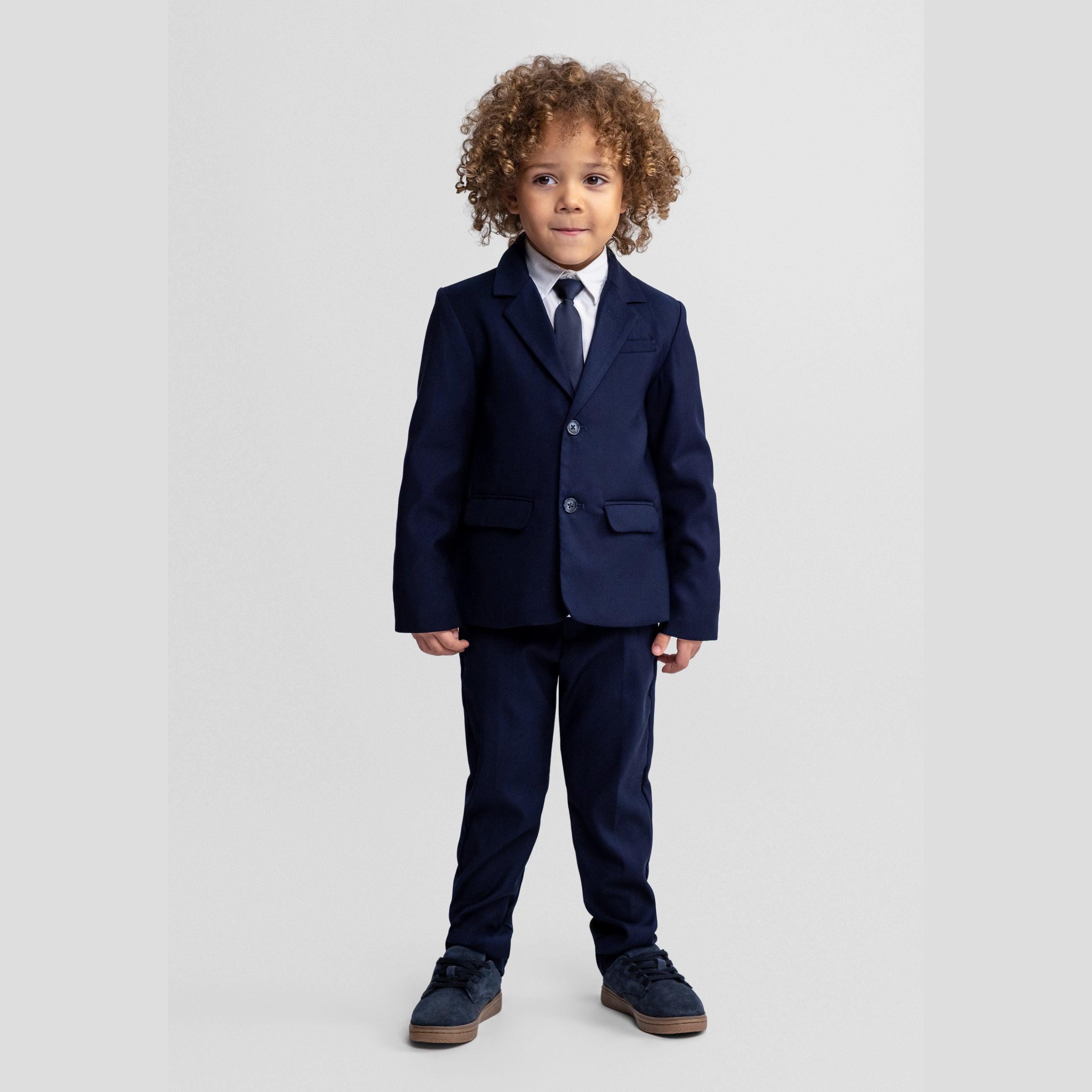 Young boy with curly hair wearing complete navy suit with tie, standing formally against white studio background