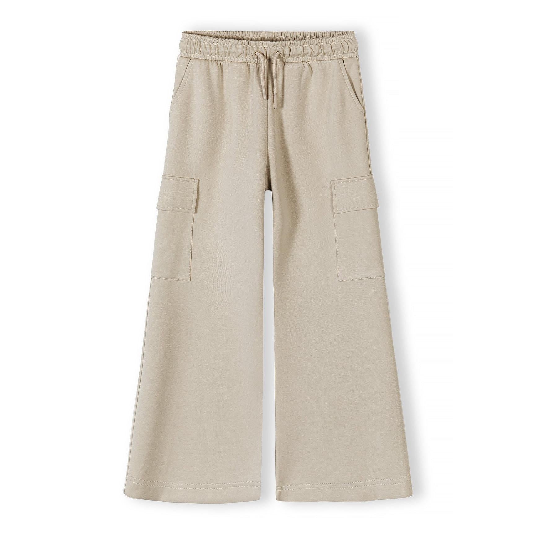 Girl in beige wide leg cargo joggers with pink puffer jacket and pink top, looking down with hands in pockets against white background