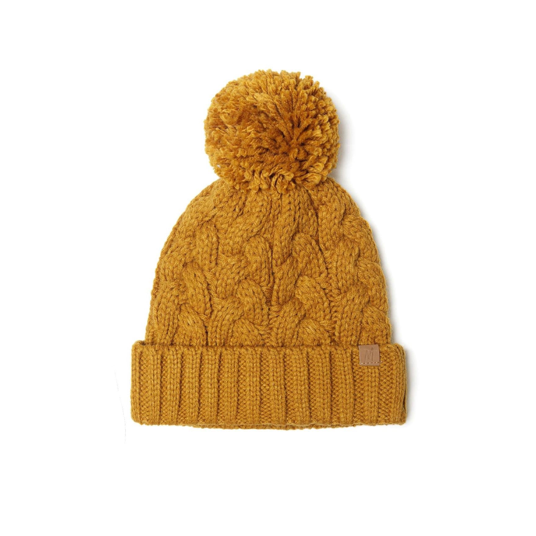 Cable knit beanie in mustard yellow with large pom pom on top, featuring textured cable pattern and ribbed cuff with leather tab, displayed on white background