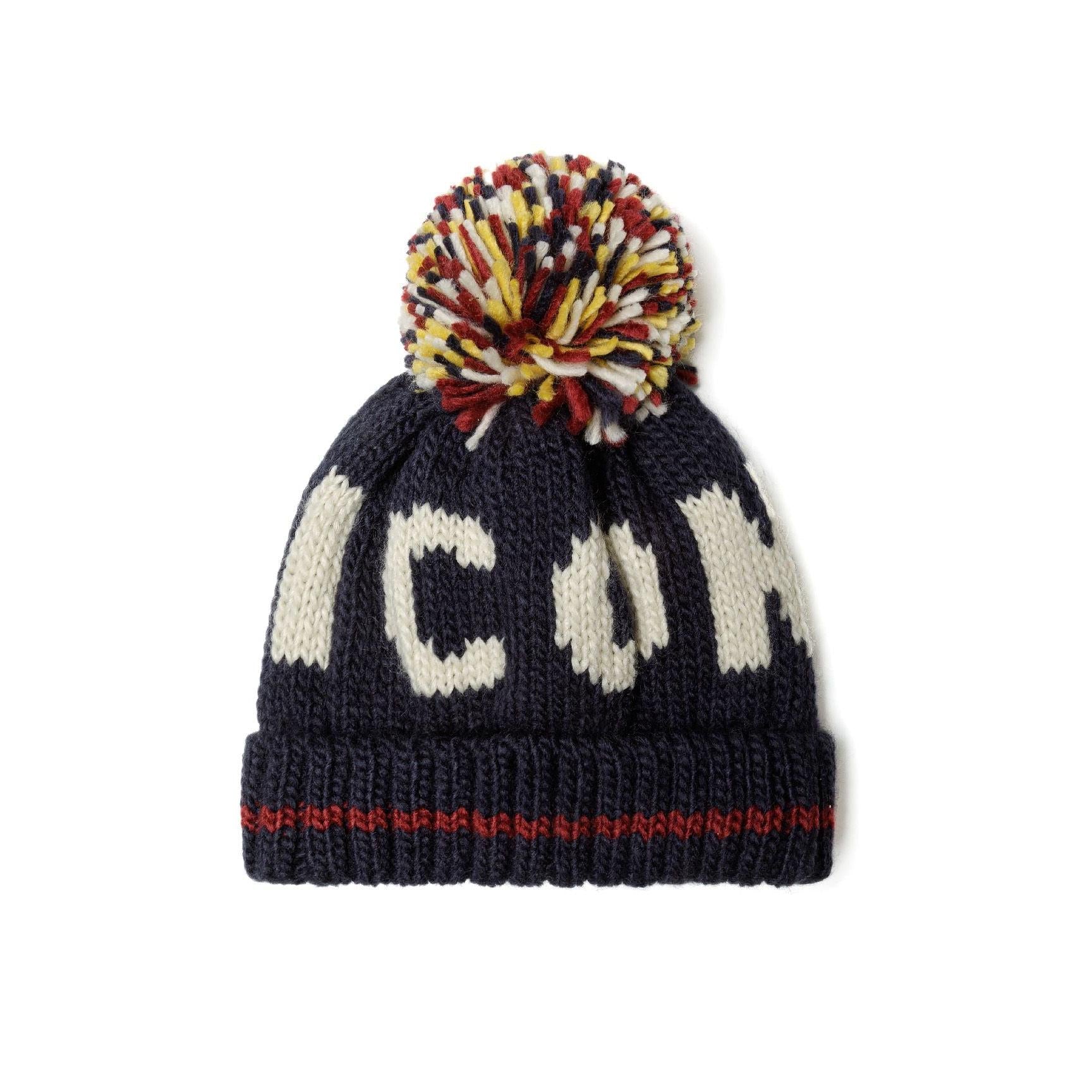 Close-up detail of navy knitted beanie showing white jacquard knit pattern and multicoloured yarn pom pom with red, yellow, white and navy strands