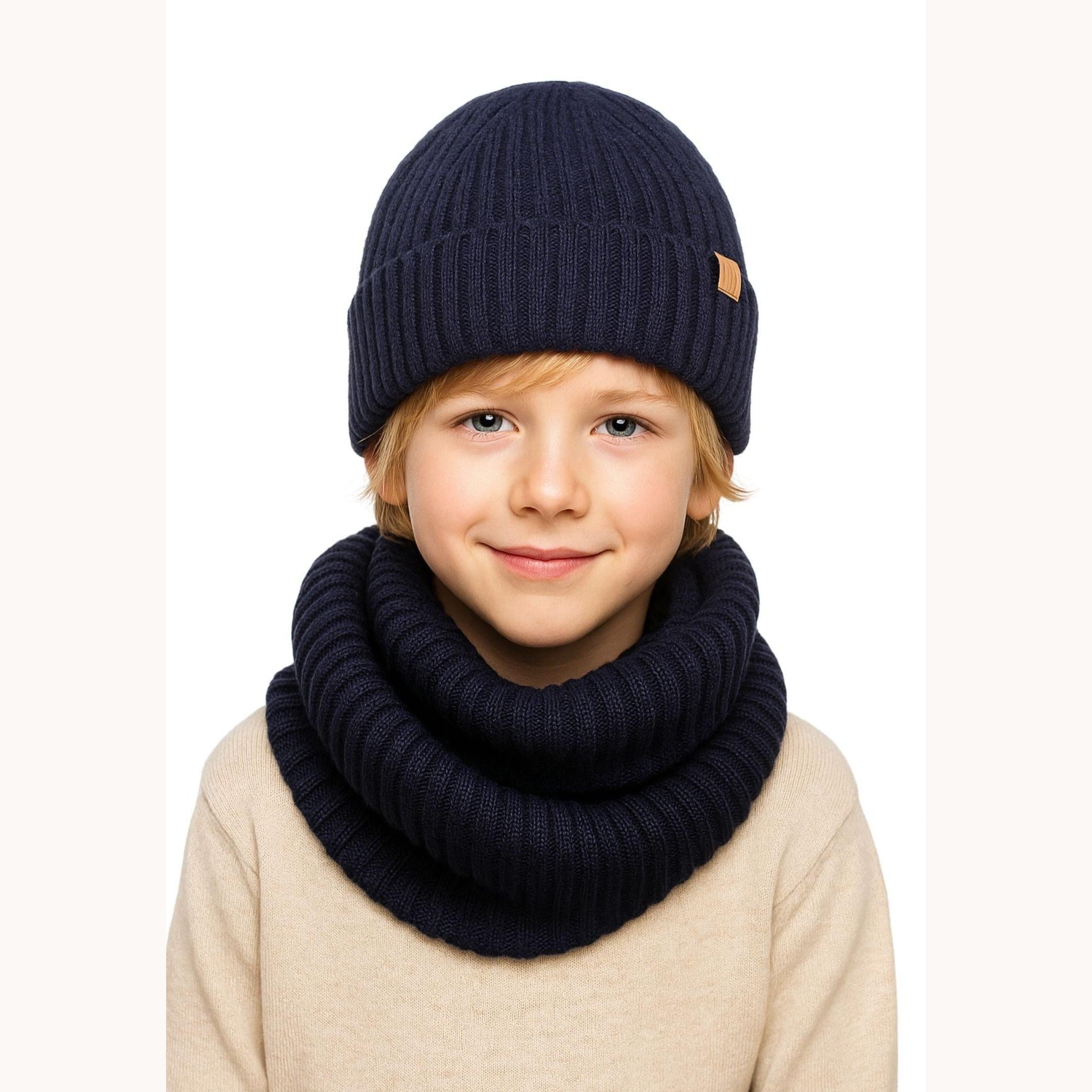 Child wearing navy ribbed knit beanie and snood set with beige sweater against white background