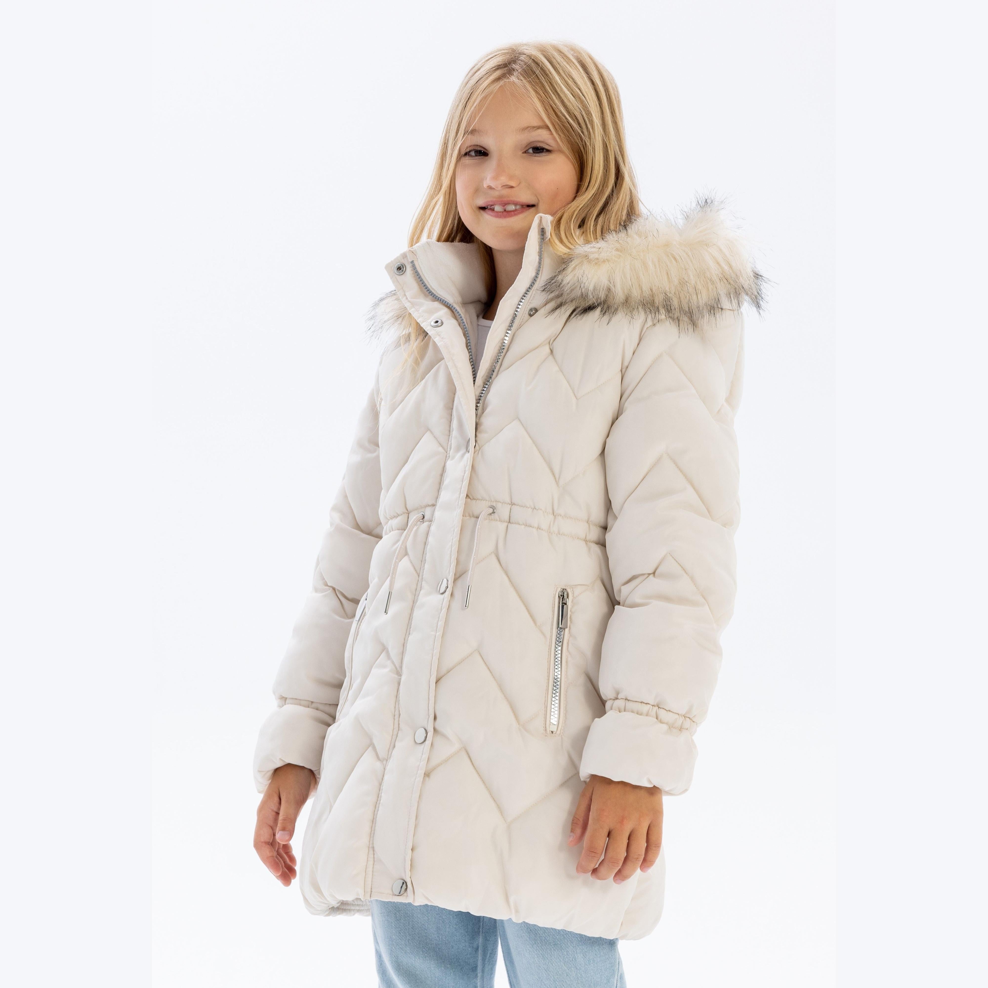 Young girl wearing cream quilted parka jacket with faux fur hood trim, full zip front and snap buttons, paired with jeans against white background