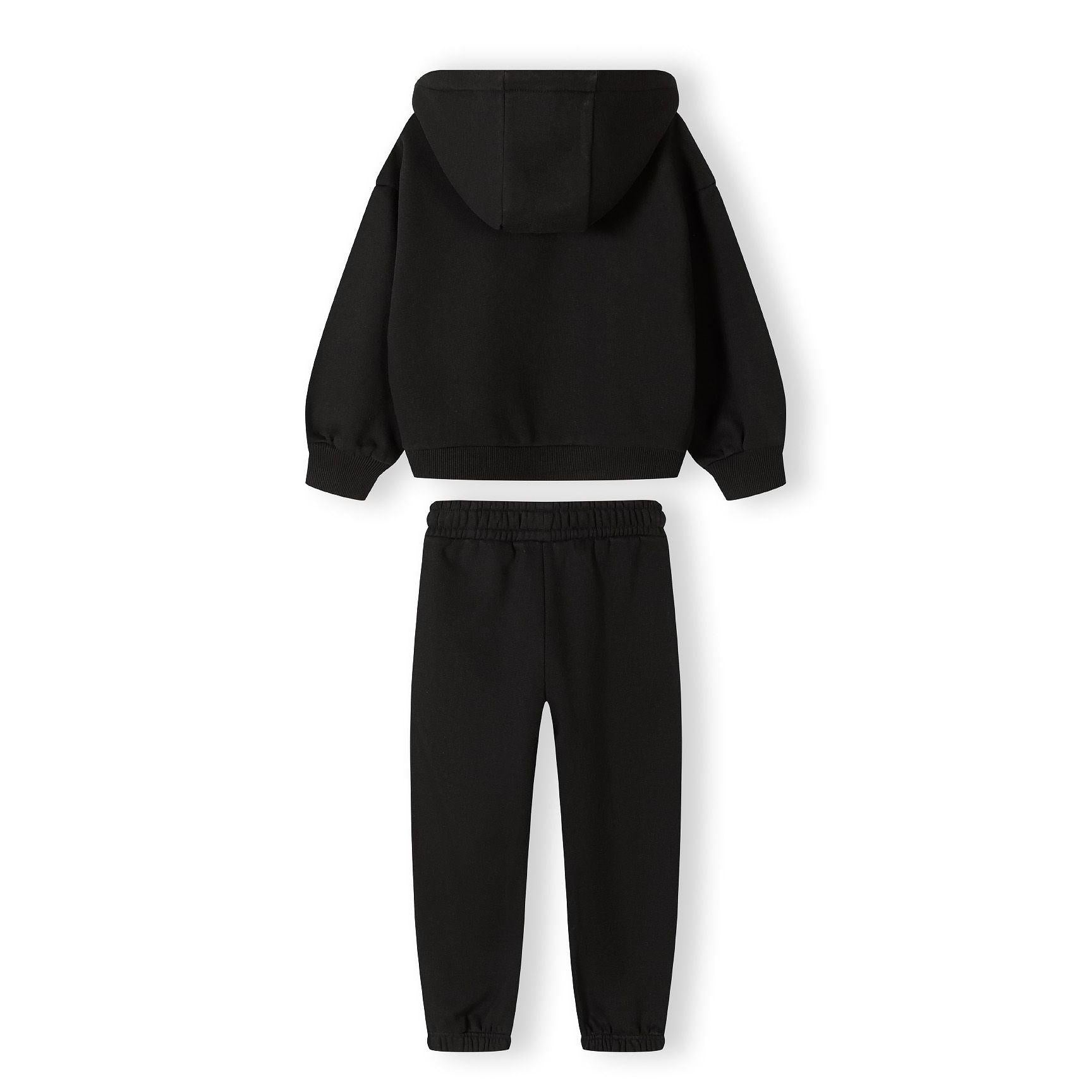 Close-up detail of black tracksuit joggers showing ribbed waistband and white text print on leg