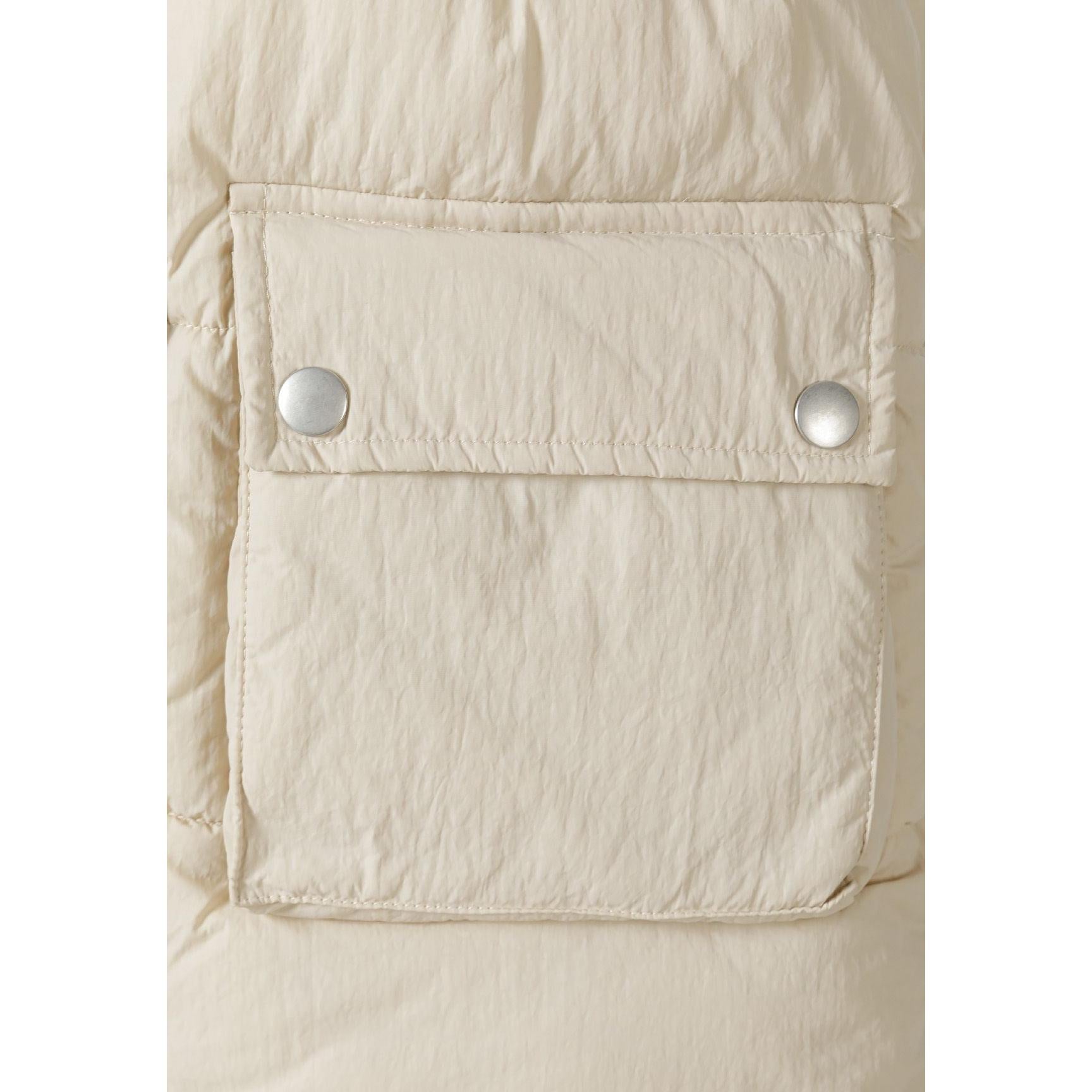 Close-up detail of cream padded gilet chest pocket with two silver snap button closures on quilted fabric