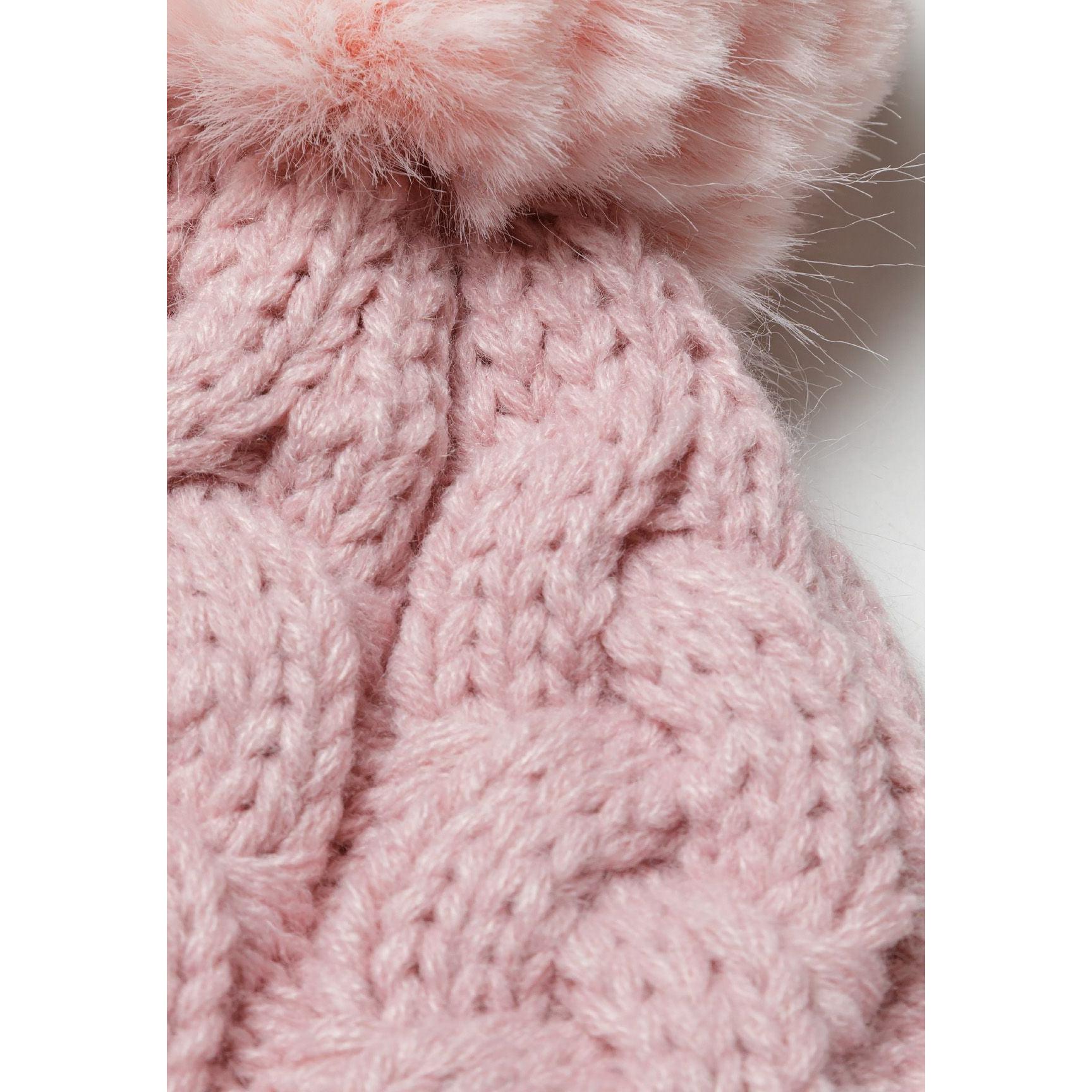 Close-up detail of light pink cable knit hat showing texture pattern and fluffy pom pom attachment