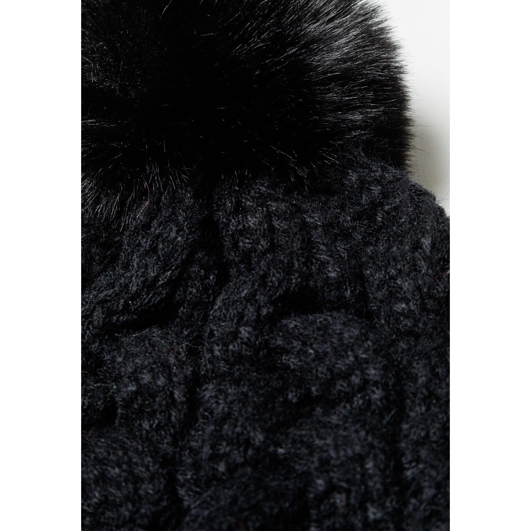Close-up detail of black cable knit hat showing textured knit pattern and fluffy black pom pom against white background