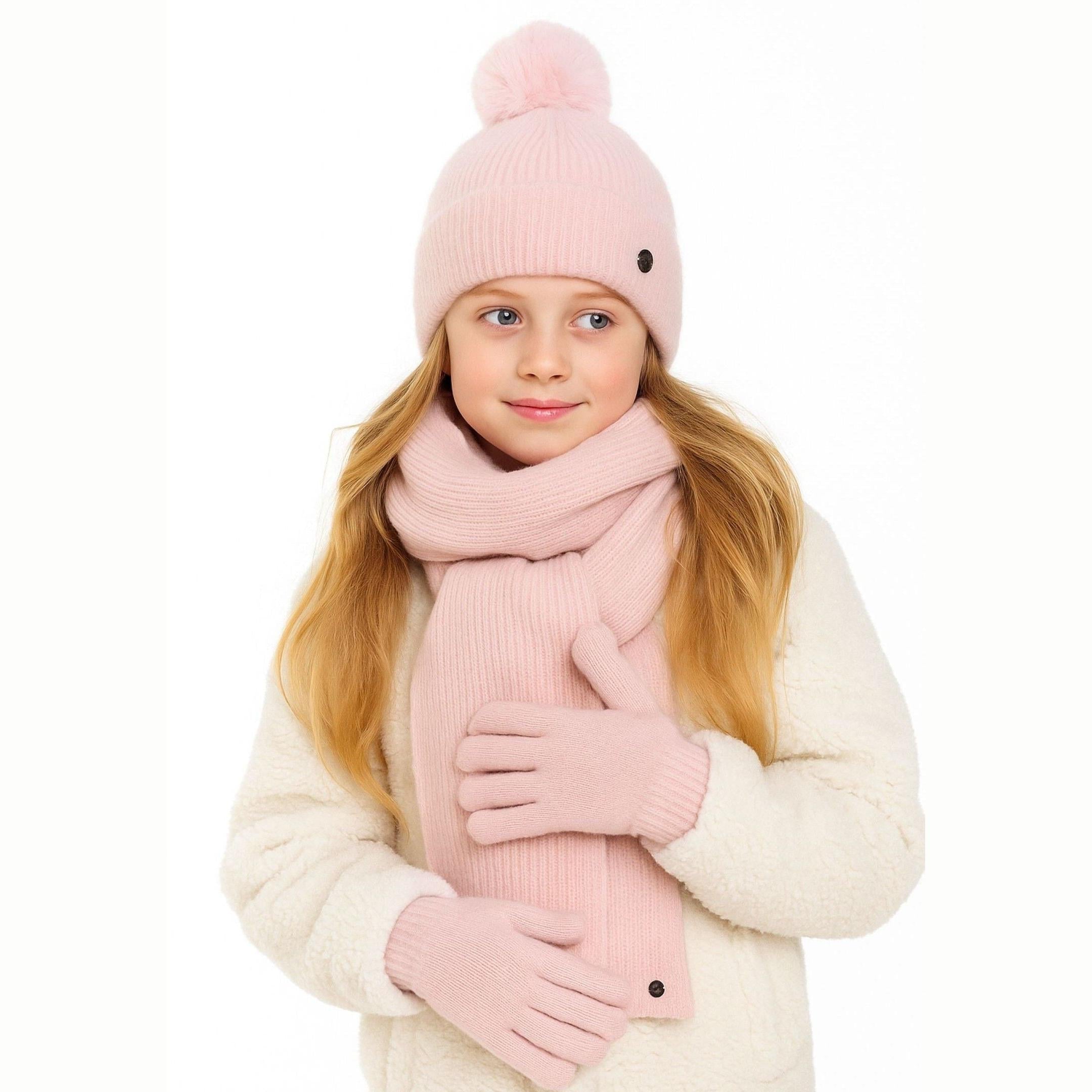 Young blonde girl wearing pale pink ribbed knit winter set with pompom hat, scarf and gloves, paired with cream fuzzy cardigan on white background