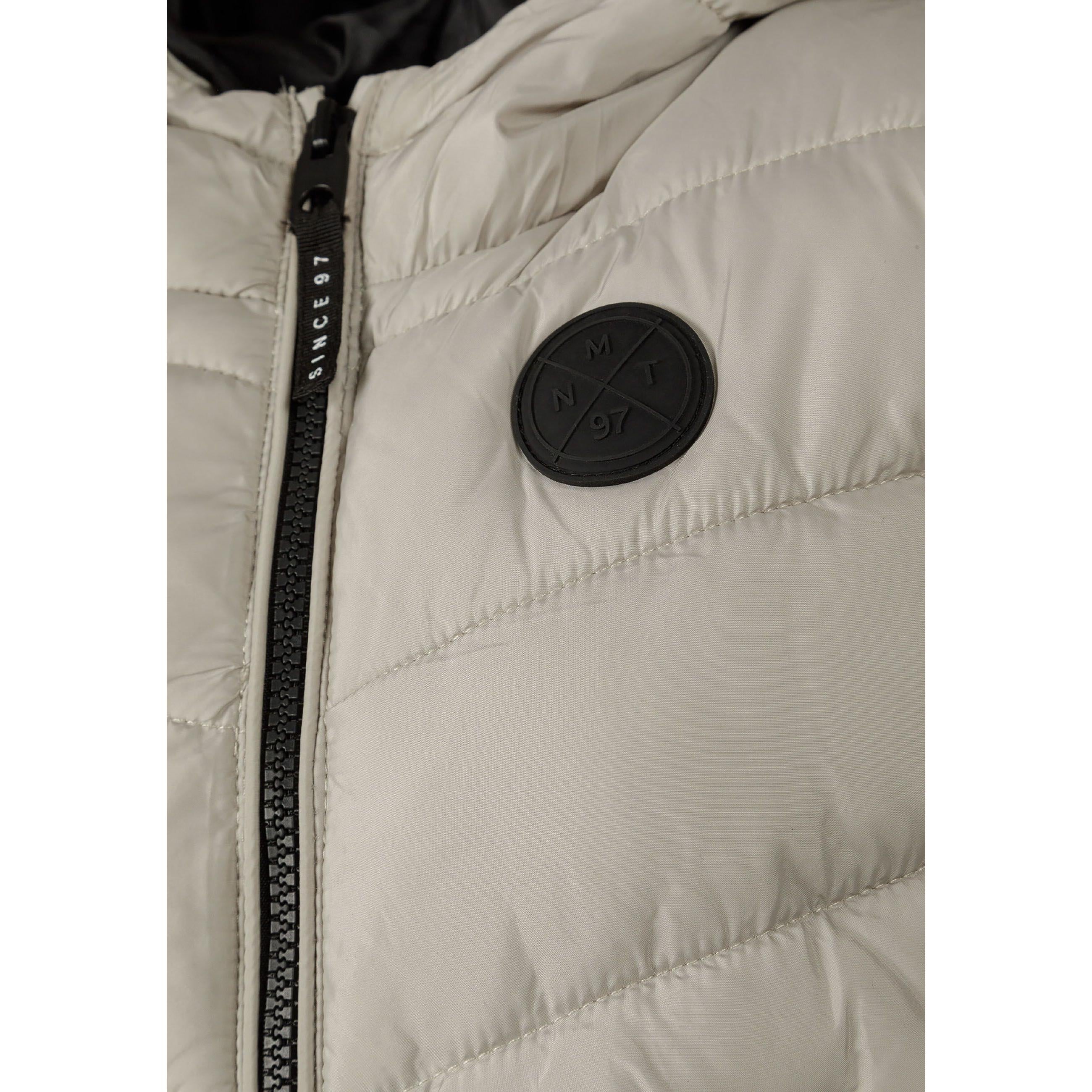 Close-up detail of grey padded gilet showing black circular Minoti logo badge and black zip with reflective zipper pull