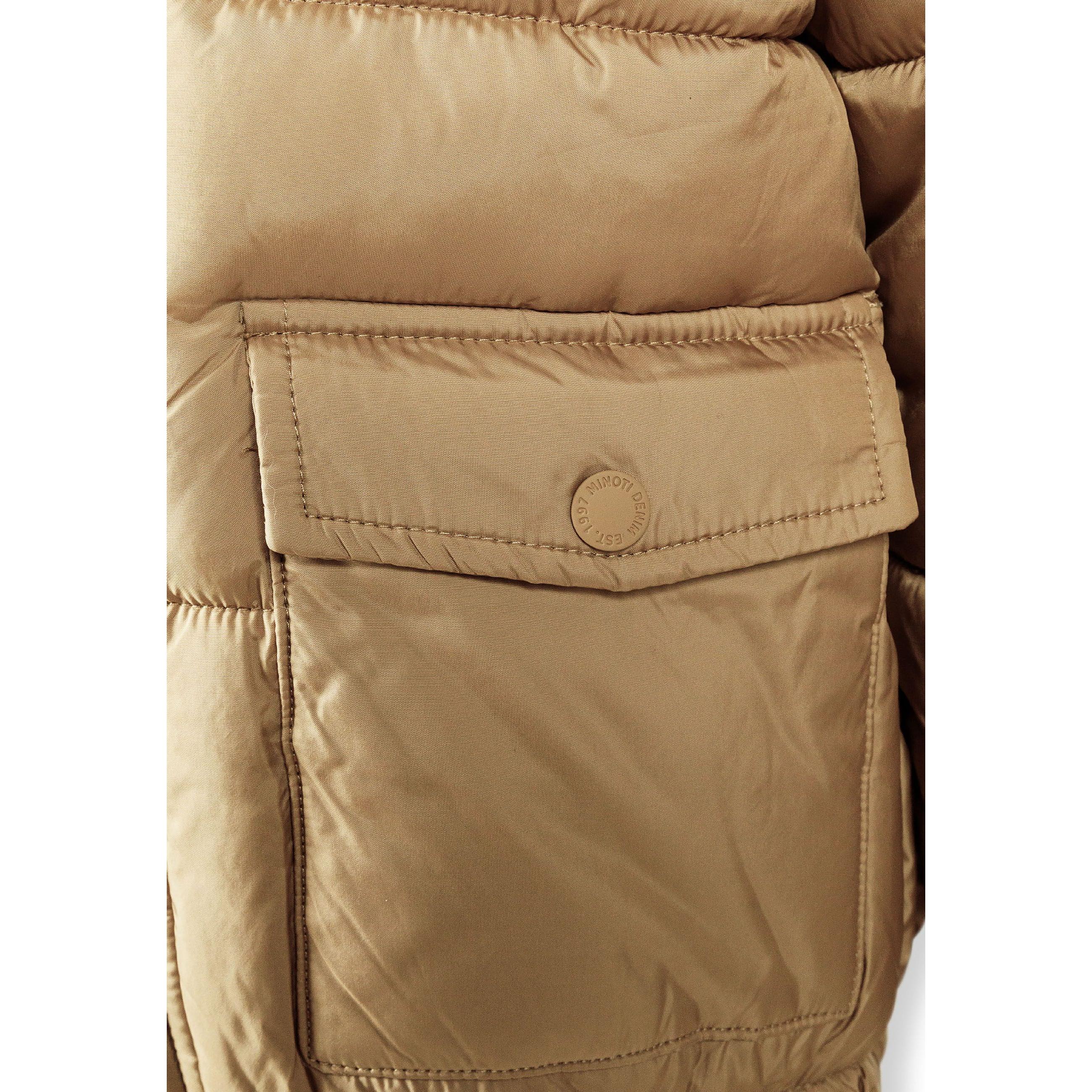 Close-up of black circular badge with white cross design showing letters M, N, T and number 97 on beige jacket fabric