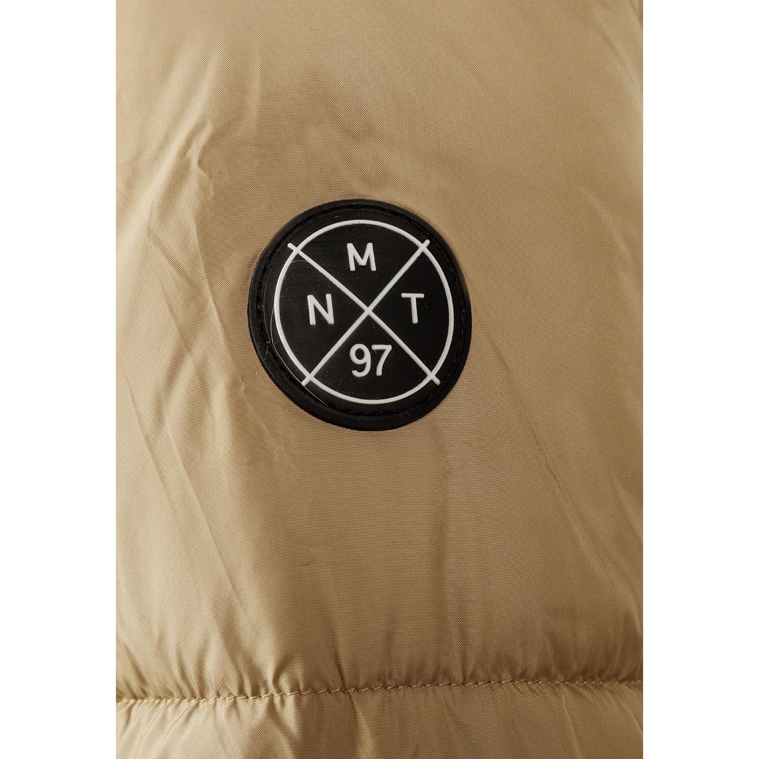 Close-up of black circular badge with white cross design showing letters M, N, T and number 97 on beige jacket fabric