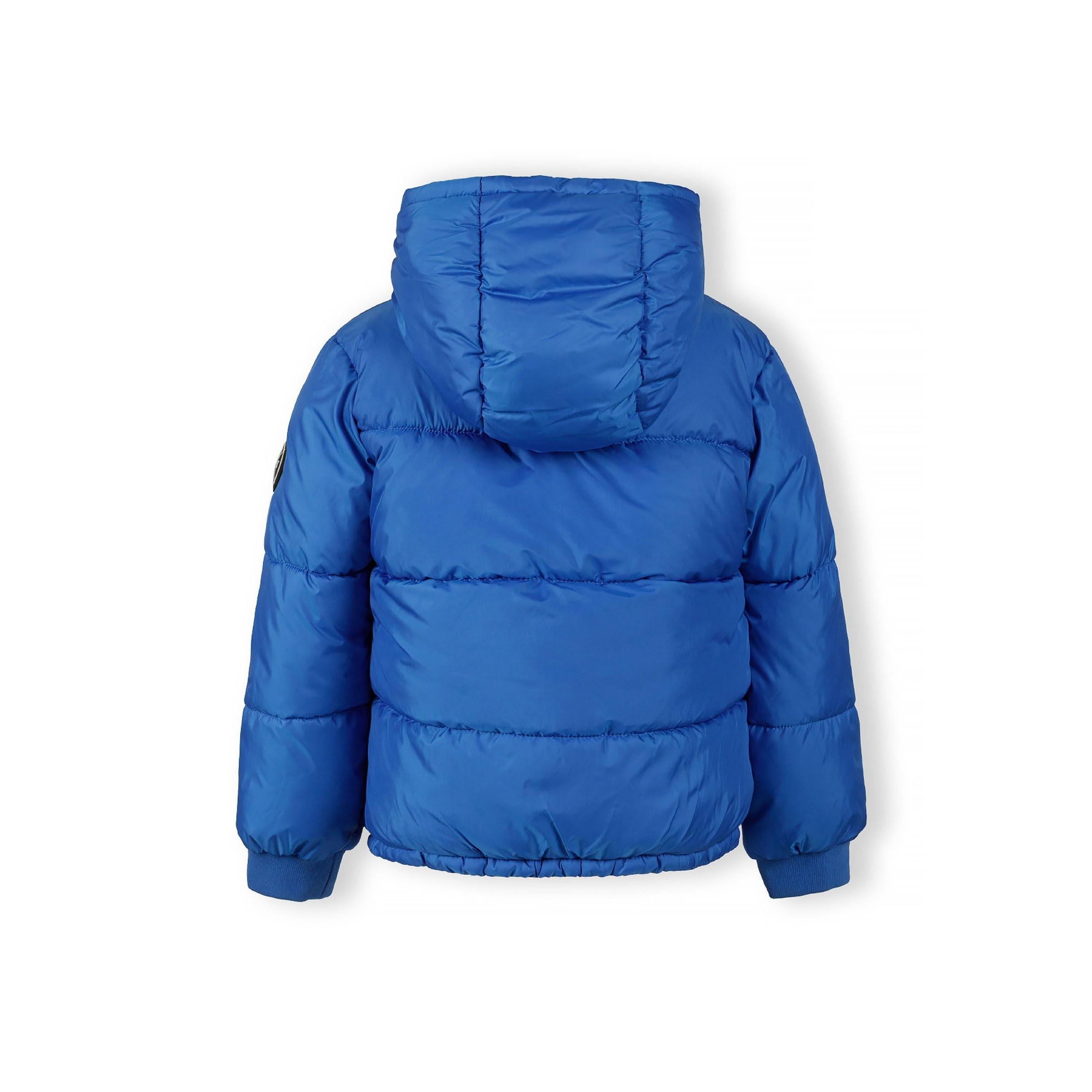 Close-up detail of cobalt blue jacket sleeve showing circular black patch with white crossed lines and letters M, N, T, 97