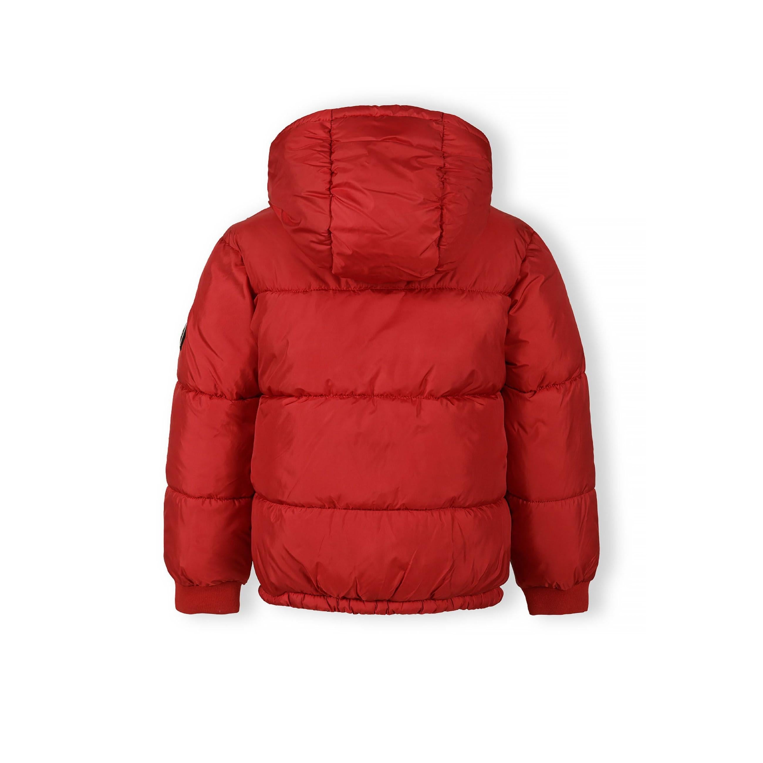 Close-up detail of black circular logo patch with white crossed lines and letters M N T 97 on red jacket sleeve