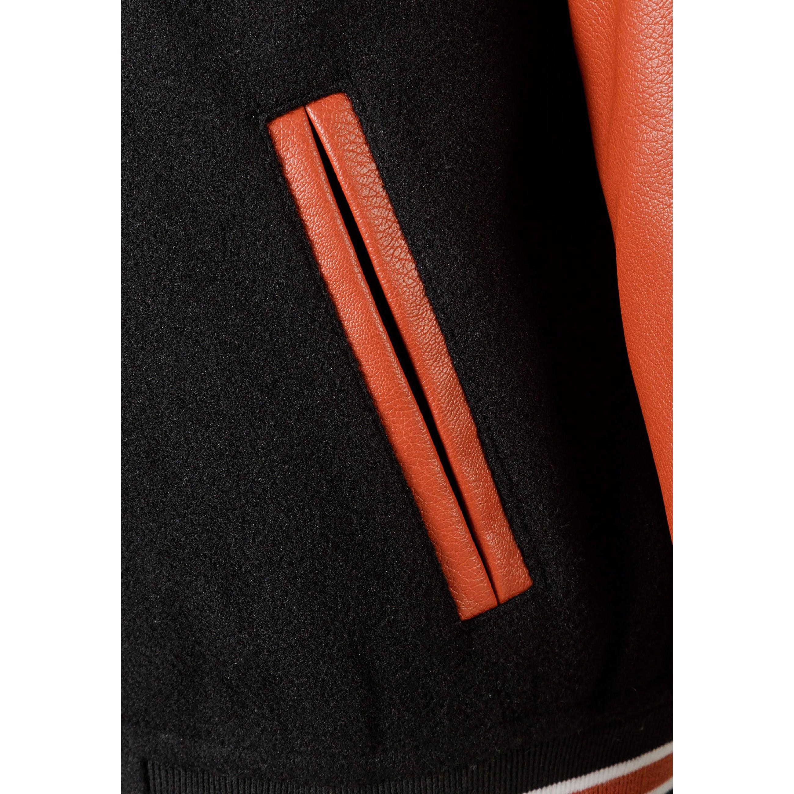 Close-up detail of orange PU leather pocket trim against black fabric body of varsity jacket, showing textured material contrast