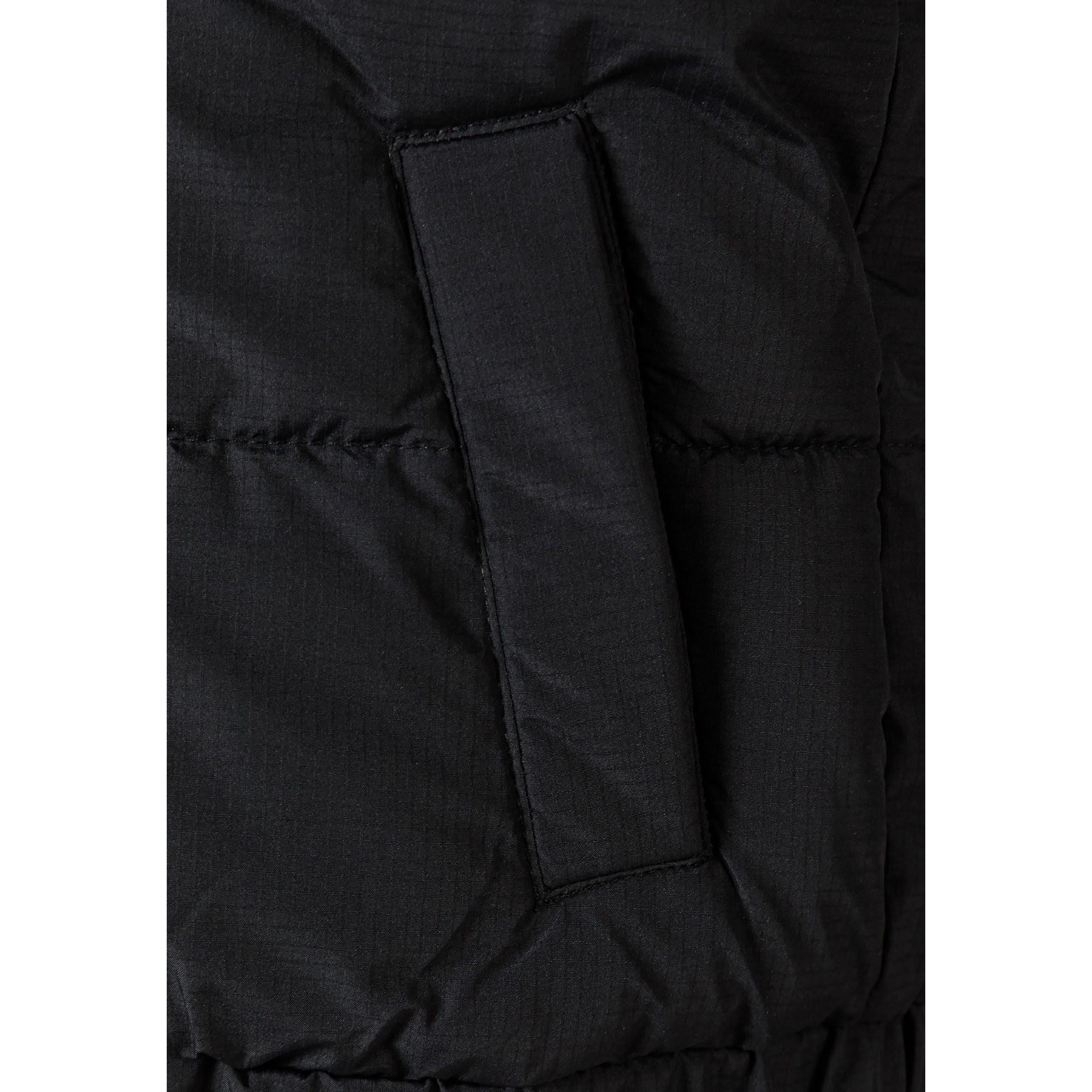 Close-up detail of black gilet showing zip pocket construction and padded quilted fabric texture