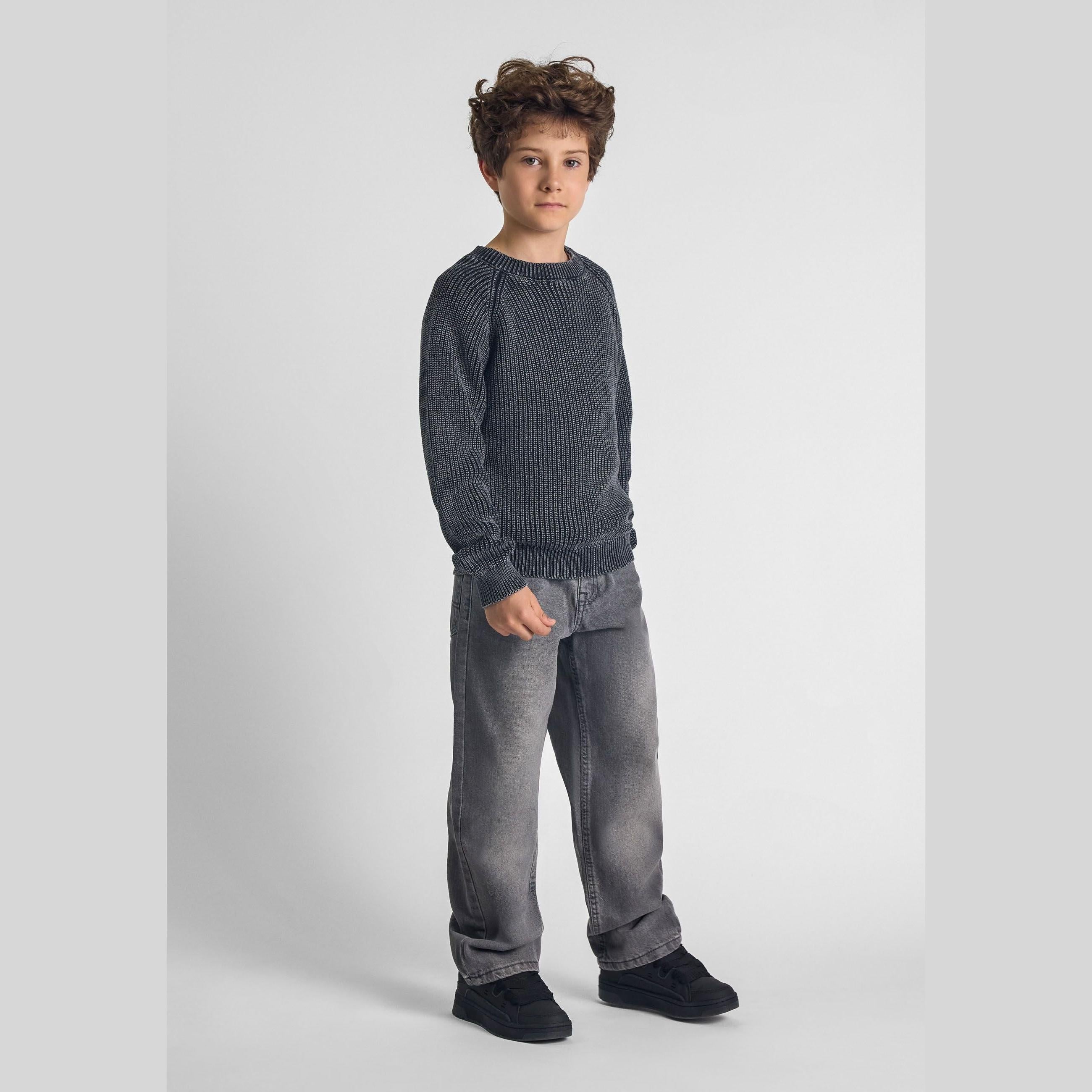 Boy wearing black acid wash raglan sleeve jumper with grey jeans against white studio background, full body front view
