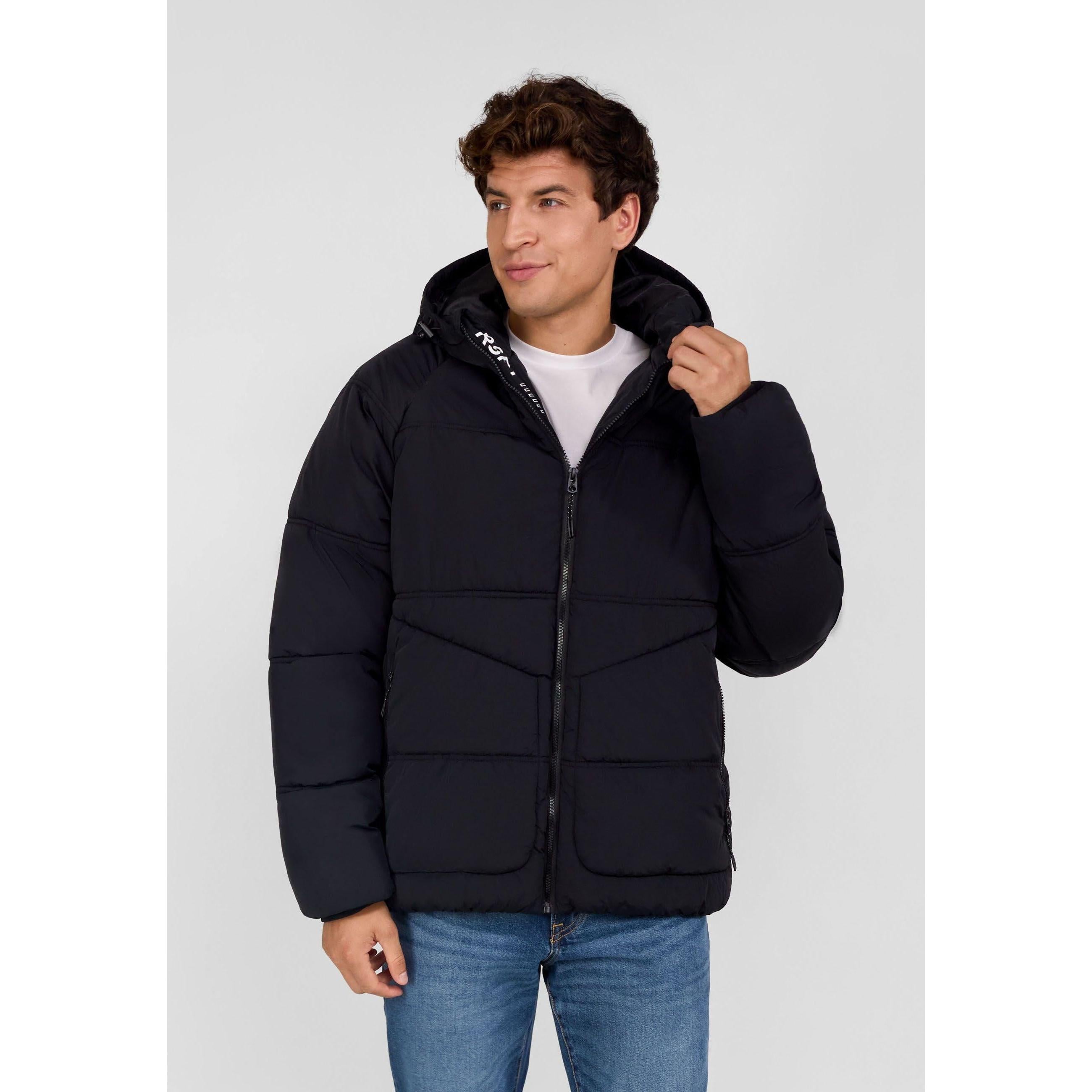 Young male model wearing navy quilted winter jacket with hood, standing against light grey background, hand adjusting hood