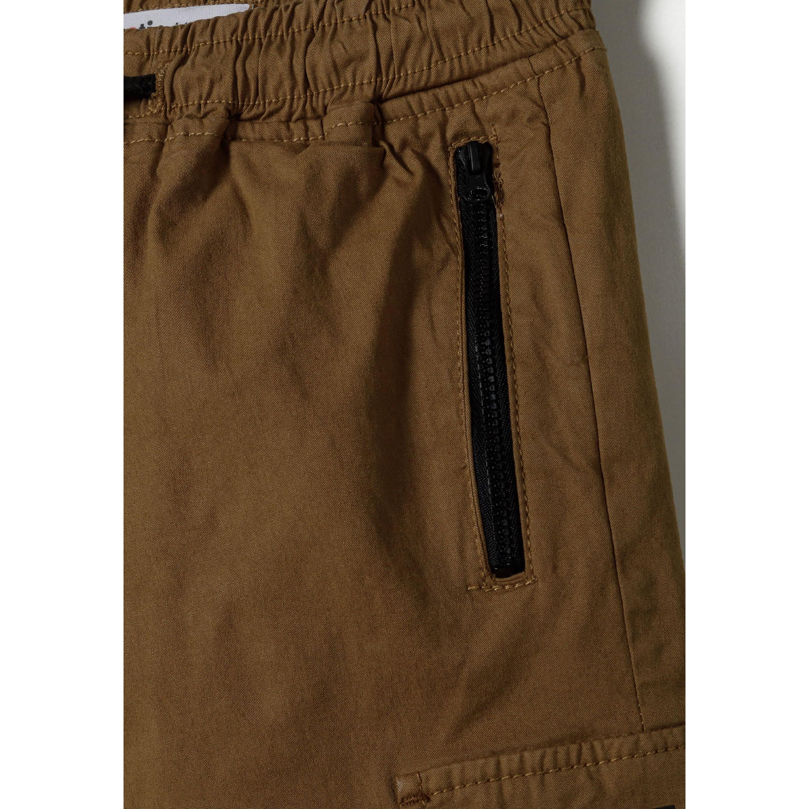 Close-up detail of beige cargo trousers showing black zip pocket closure and elasticated waistband construction