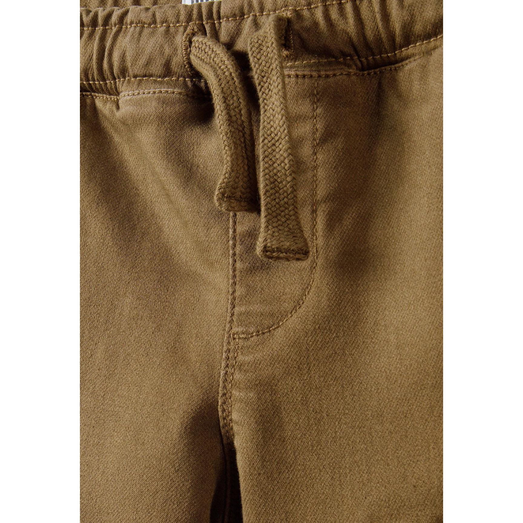 Close-up detail of brown knitted cargo trousers showing drawstring waist ties and front waistband construction