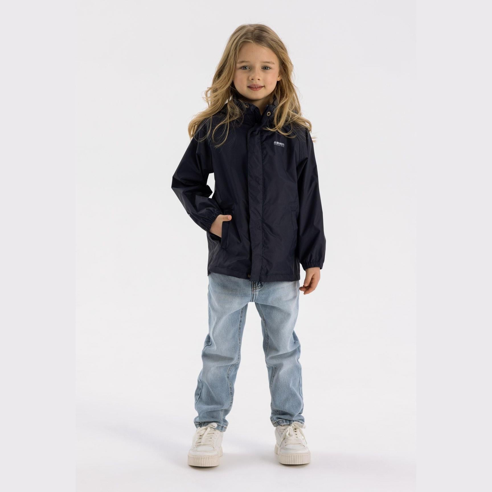Young girl wearing navy packaway waterproof jacket with hood up, paired with light blue jeans and white trainers, standing against white background