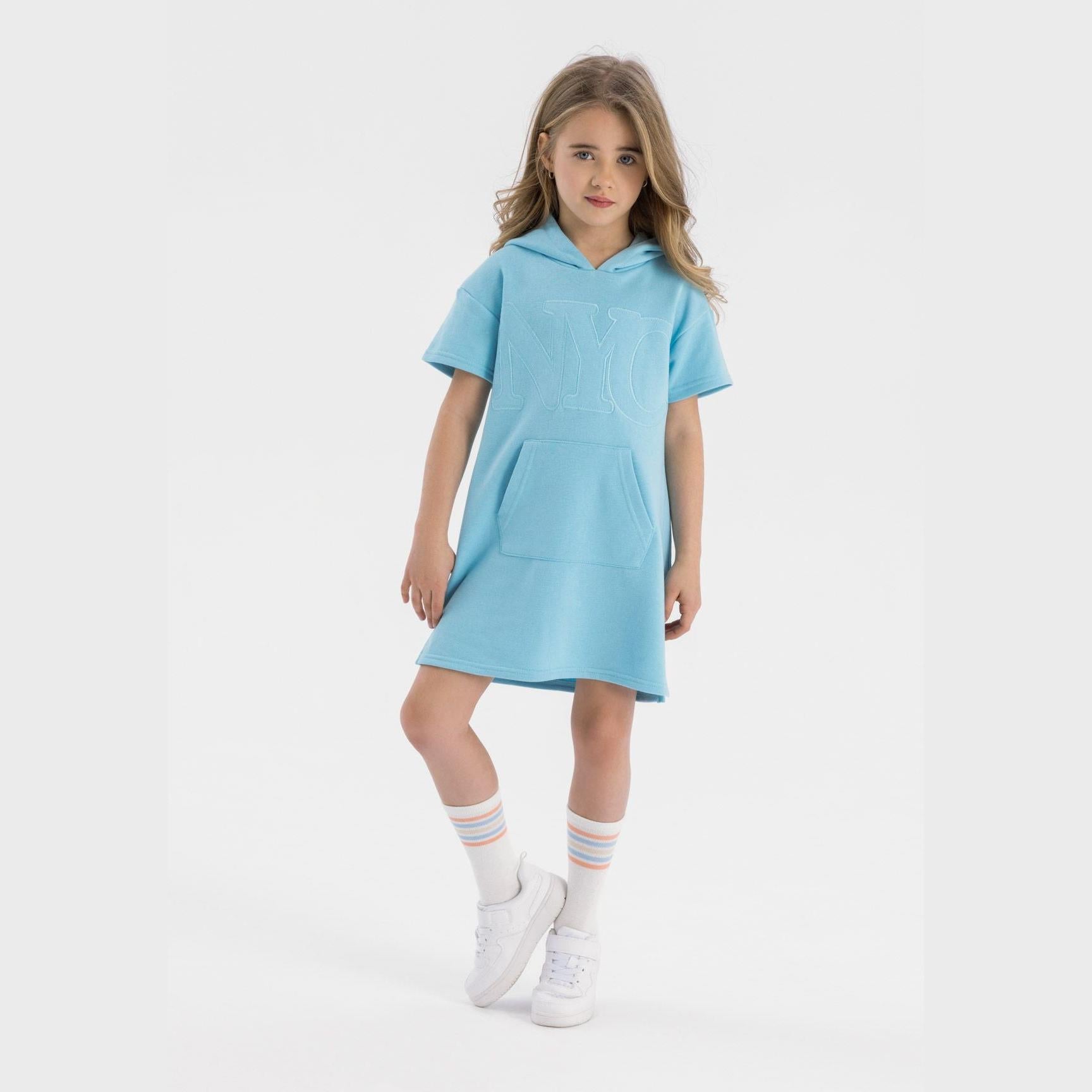 Girl wearing light blue cotton fleece hooded dress with short sleeves, white striped socks and white sneakers, standing against white background