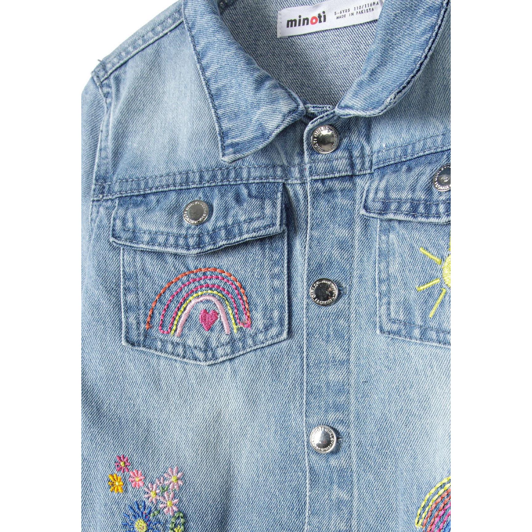 Close-up detail of light blue denim jacket showing Minoti label, rainbow embroidery on chest pocket, and navy contrast cuffs with white polka dots