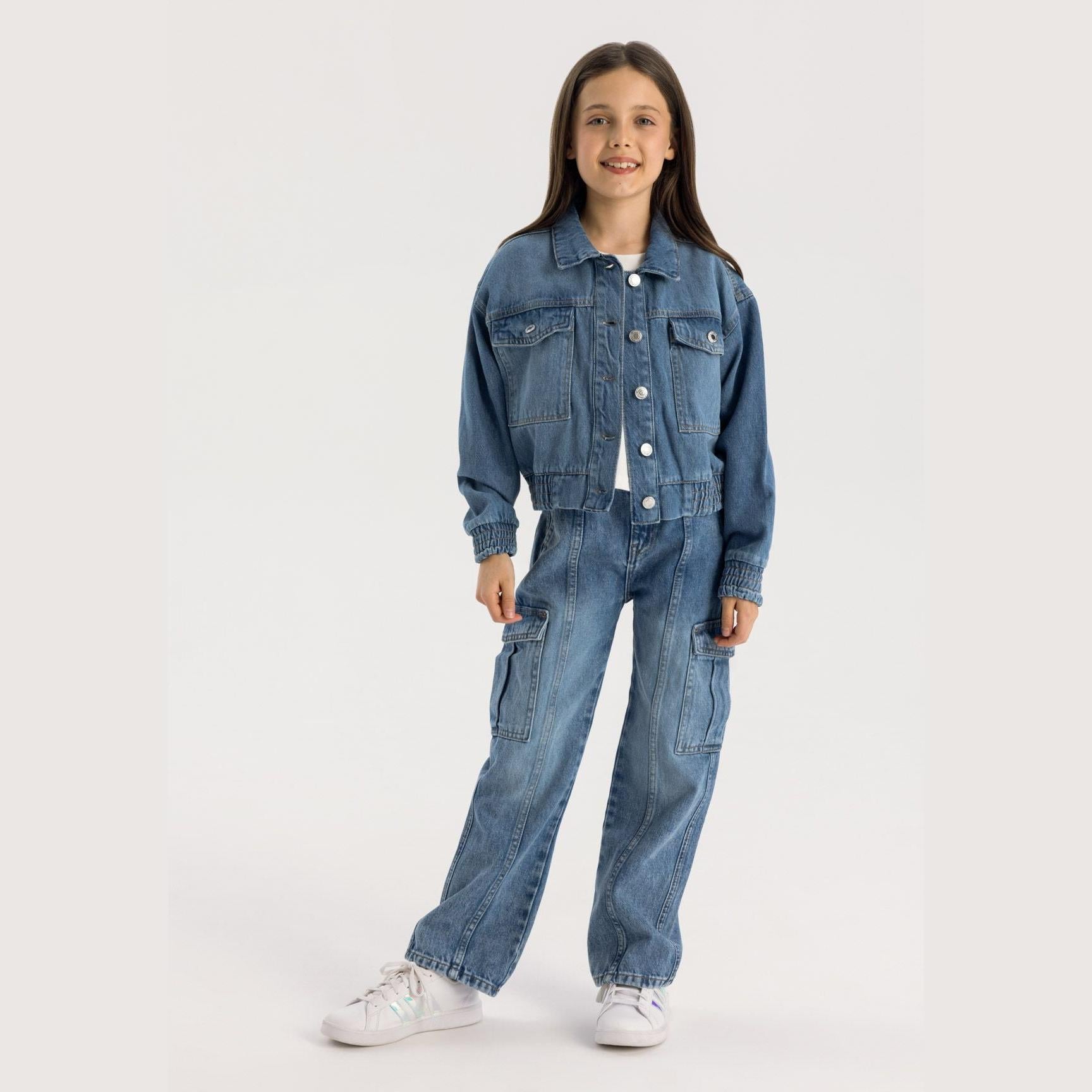 Young girl wearing navy cropped denim jacket with matching cargo trousers, standing against white background, full body front view