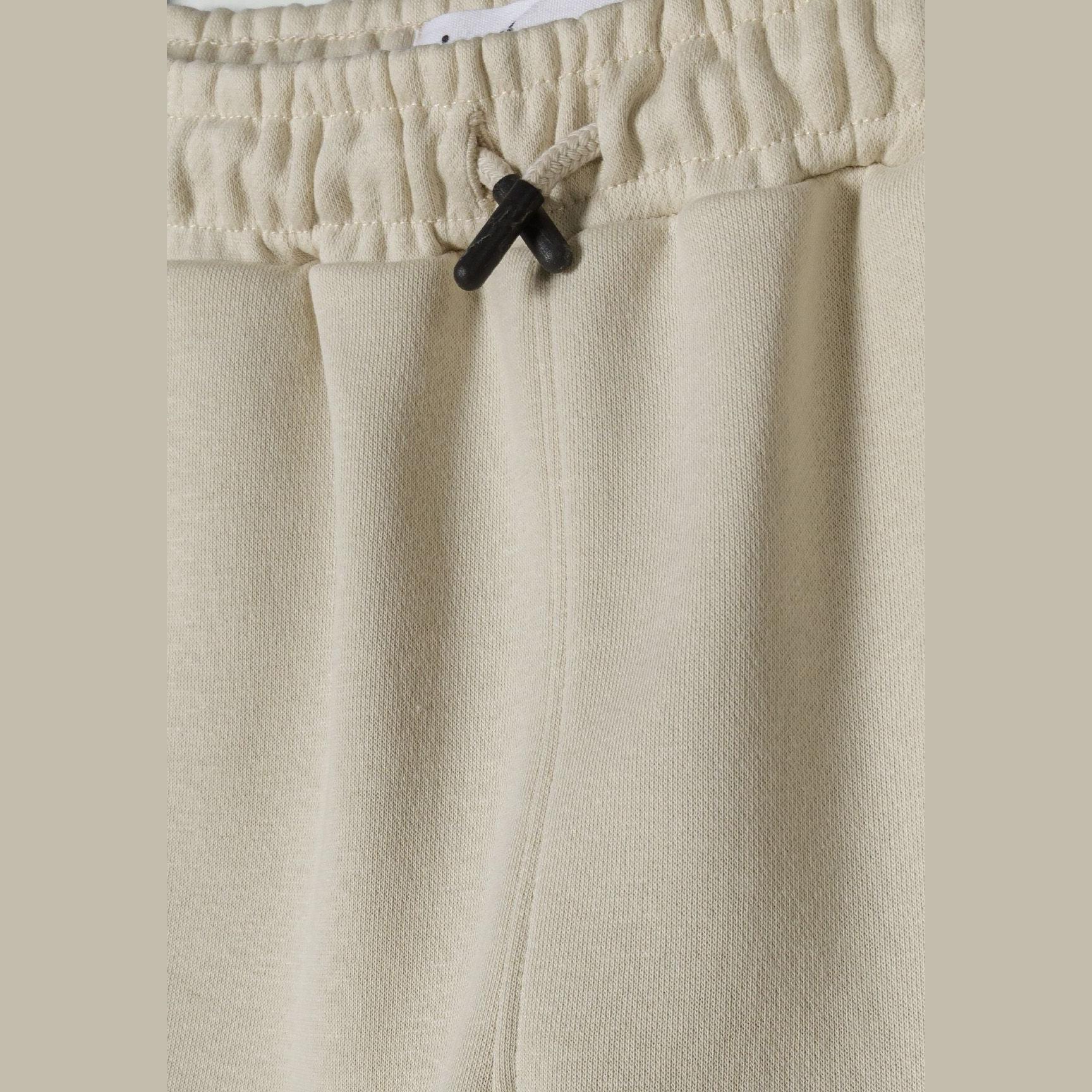 Close-up detail of beige shorts waistband showing elasticated fabric and black drawstring toggle