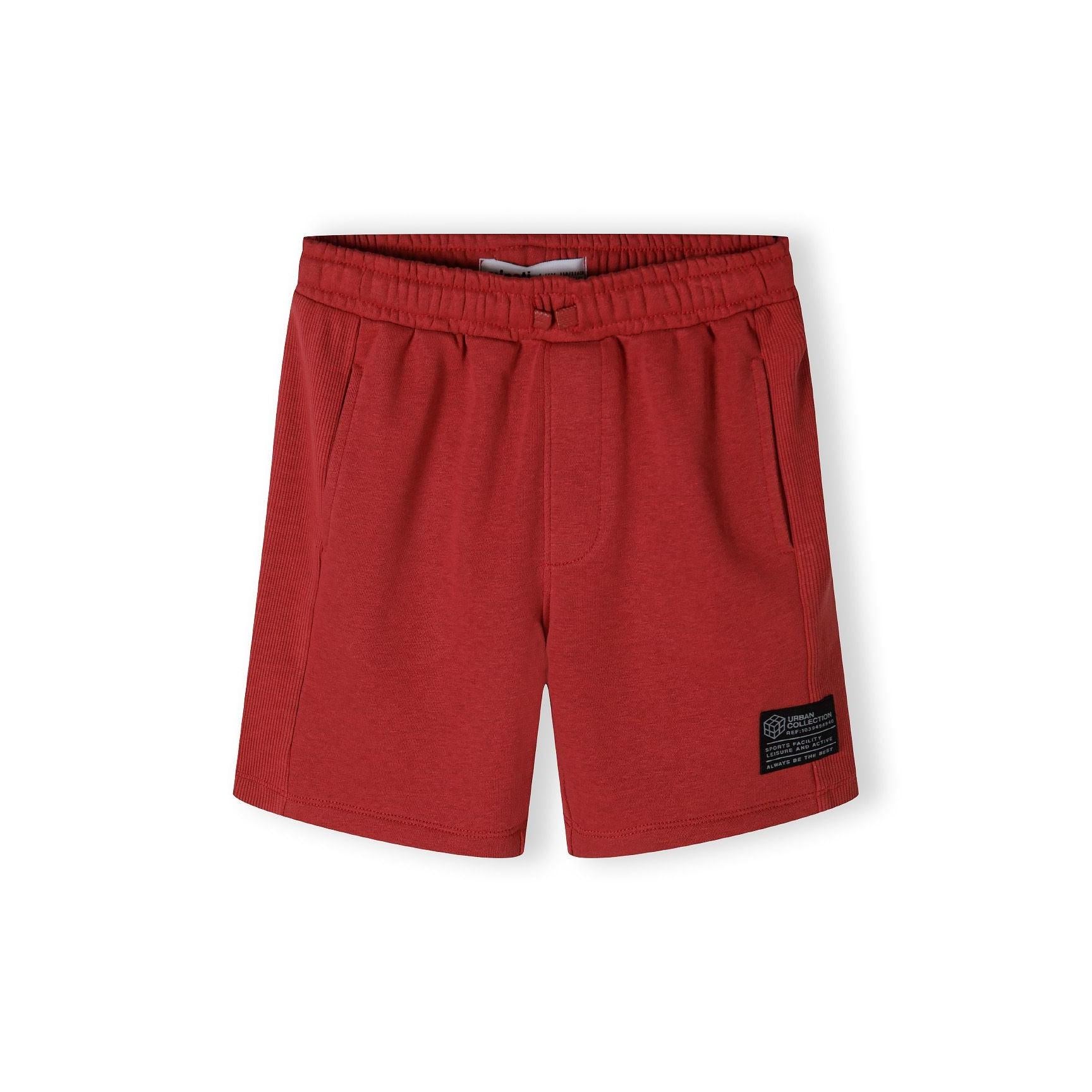Red fleece shorts laid flat showing elastic waistband, relaxed fit and ribbed fabric side panels against clean white background