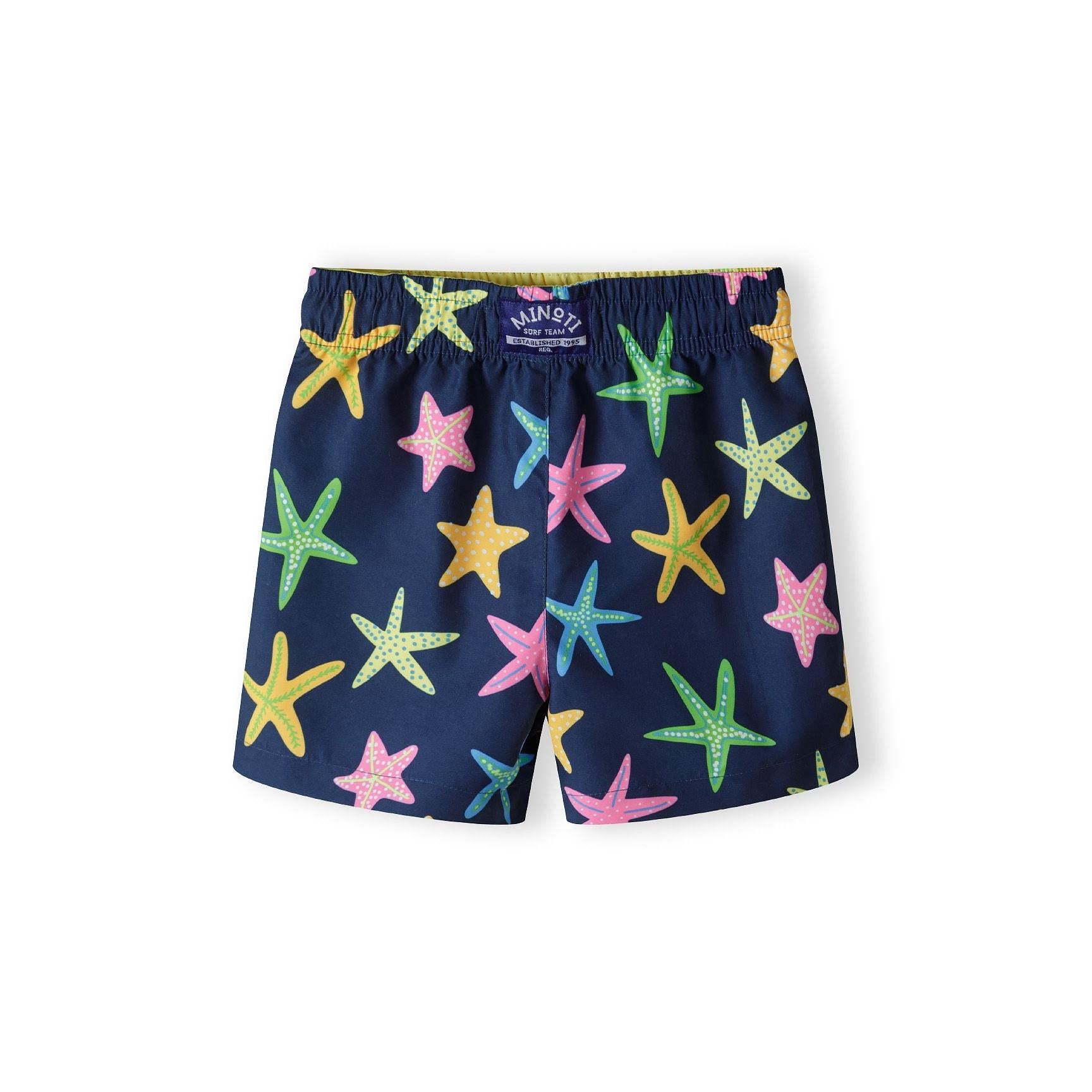 Back view of navy starfish print board shorts showing Minoti brand label at waistband and continued colourful starfish pattern across the garment on white background