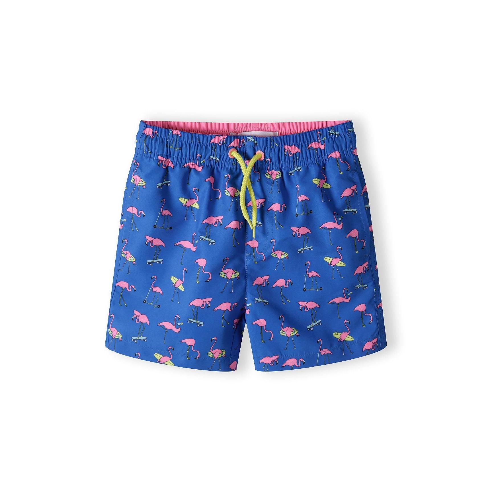 Cobalt blue board shorts with pink flamingo print pattern laid flat against white background, showing full front view with yellow drawstring