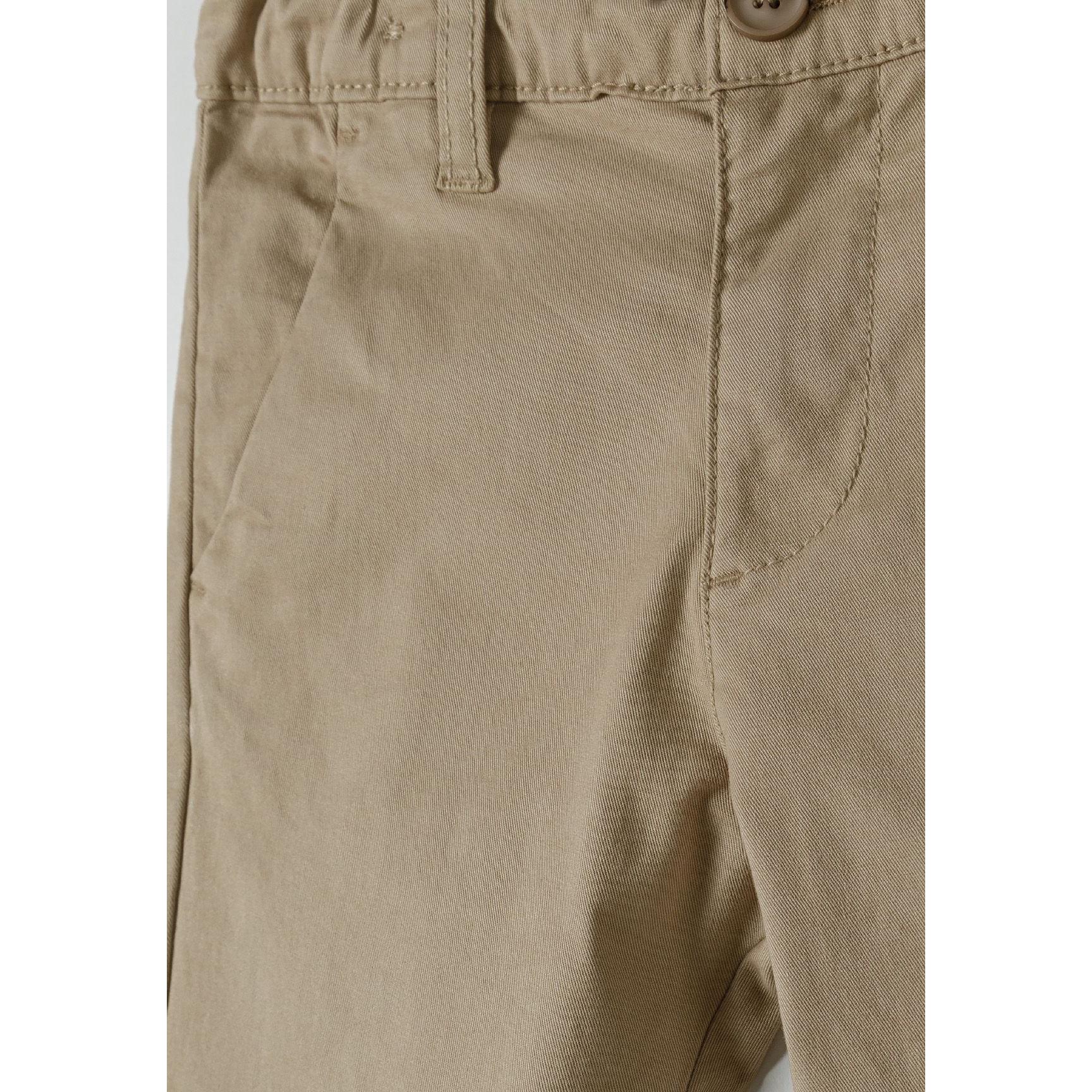 Close-up detail of beige chino trousers showing waistband, button fastening and front pocket construction