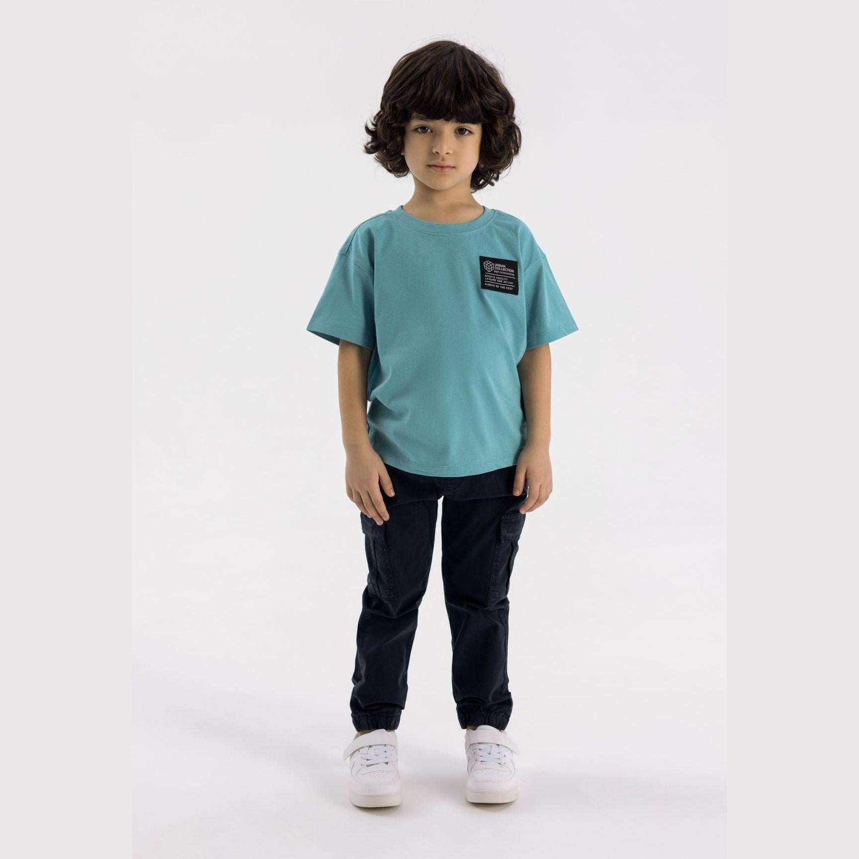 Young child wearing navy cargo trousers with aqua blue t-shirt, standing against white background, showing full outfit styling