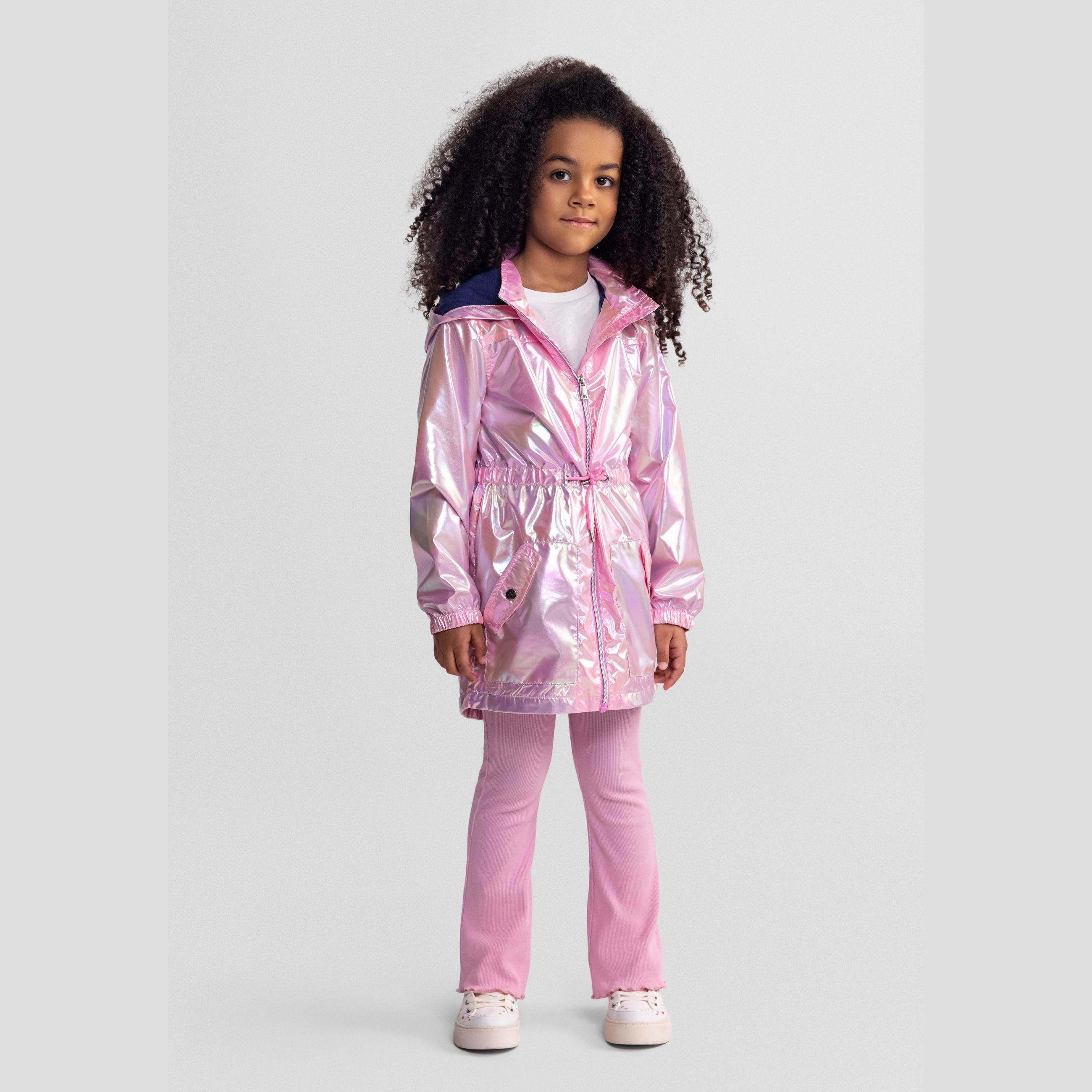 Young girl wearing iridescent pink hooded jacket with navy hood lining and matching pink leggings, standing against white background