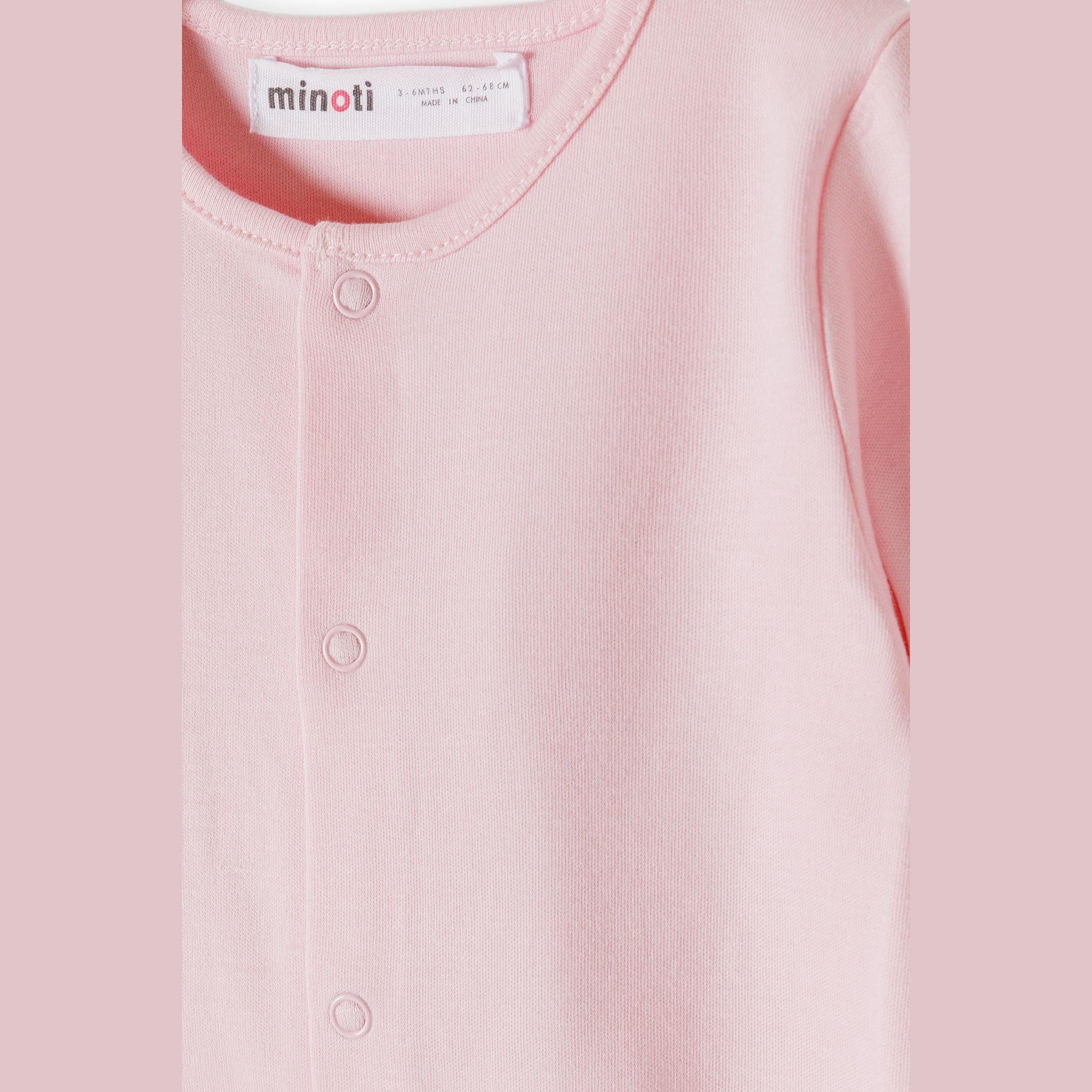 Close-up detail of pink sleepsuit showing Minoti brand label and snap button fastening system along the front opening