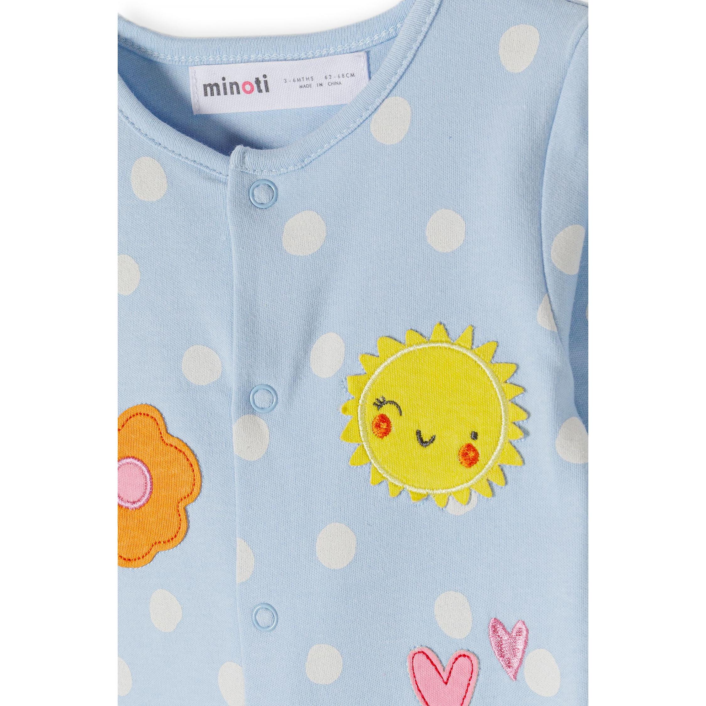 Detail shot of light blue polka dot sleepsuit showing Minoti label, press stud fastening and embroidered yellow sun with orange flower appliqués