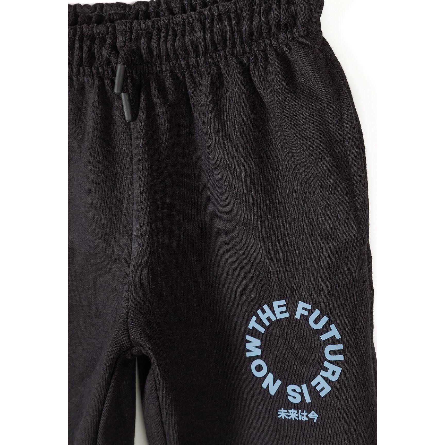 Close-up detail of black joggers showing elastic waistband with drawstring and circular printed text design featuring Japanese characters