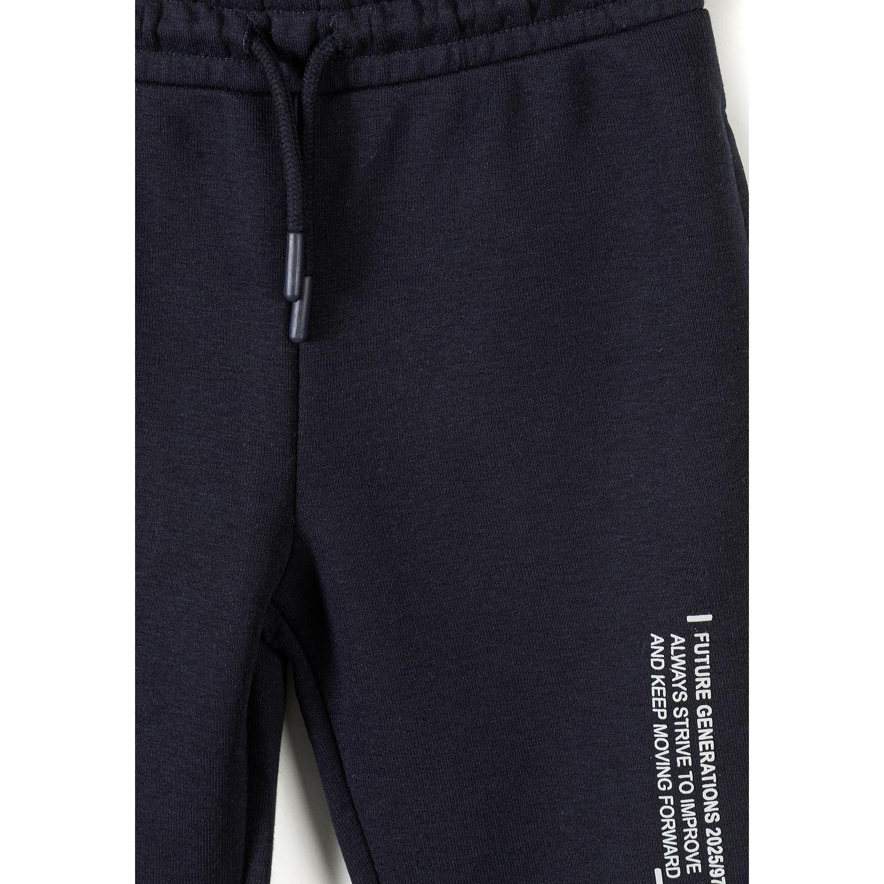 Detail view of black joggers showing drawstring waistband and vertical text print on the leg against white background
