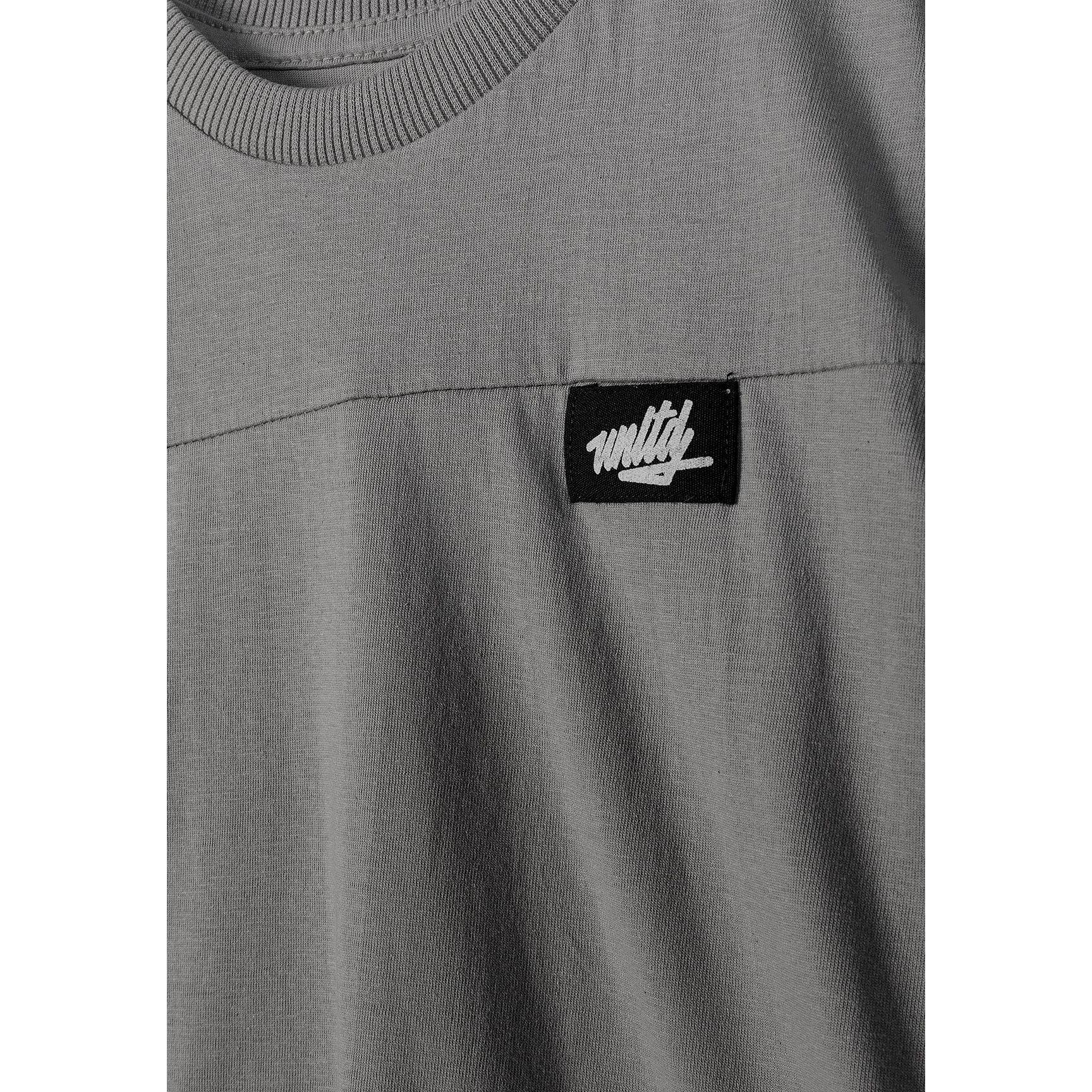 Close-up detail of black fabric label with white Minoti logo on grey t-shirt chest area