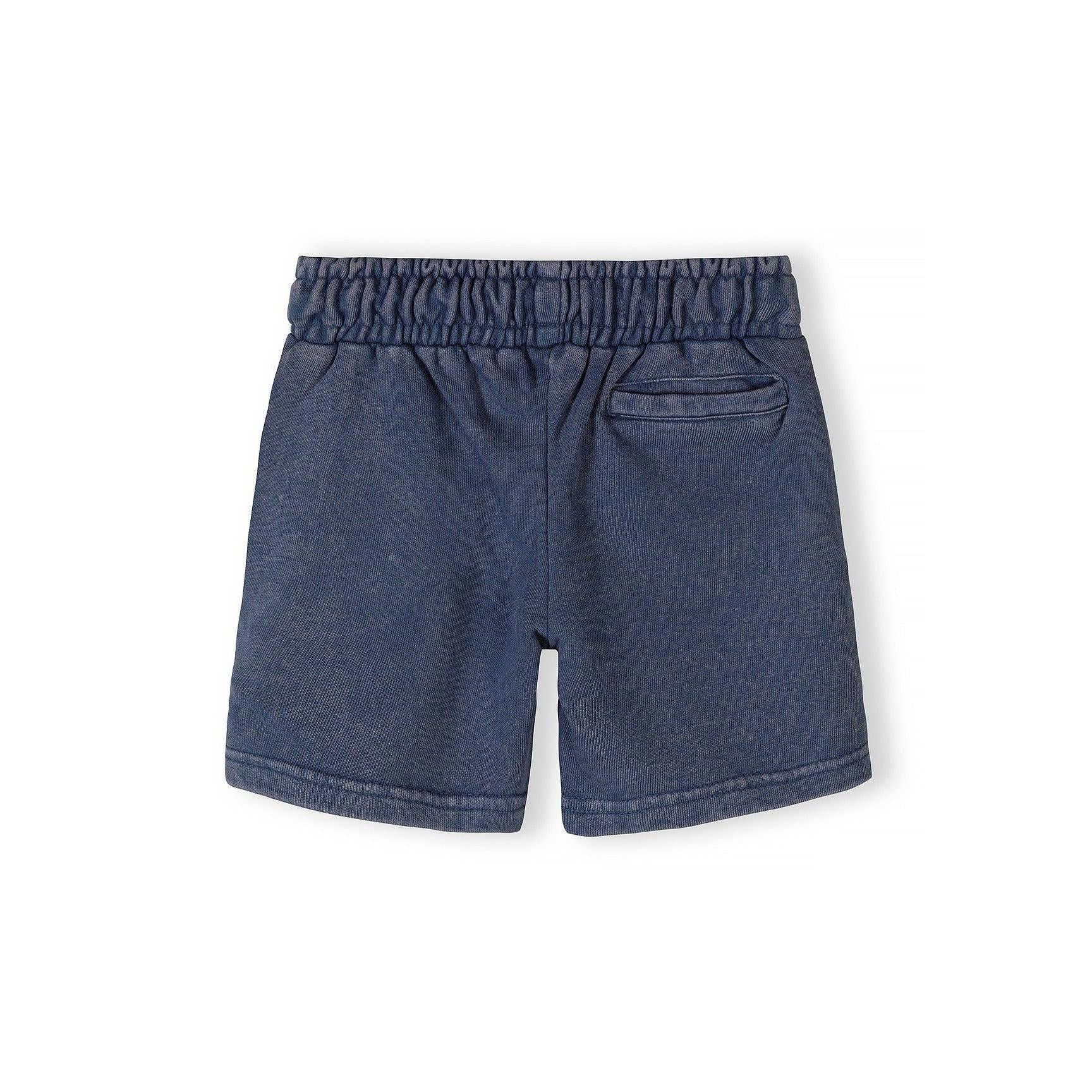 Close-up detail of blue acid wash shorts waistband showing Minoti label and 'The Future is Just Starting' text with Korean translation