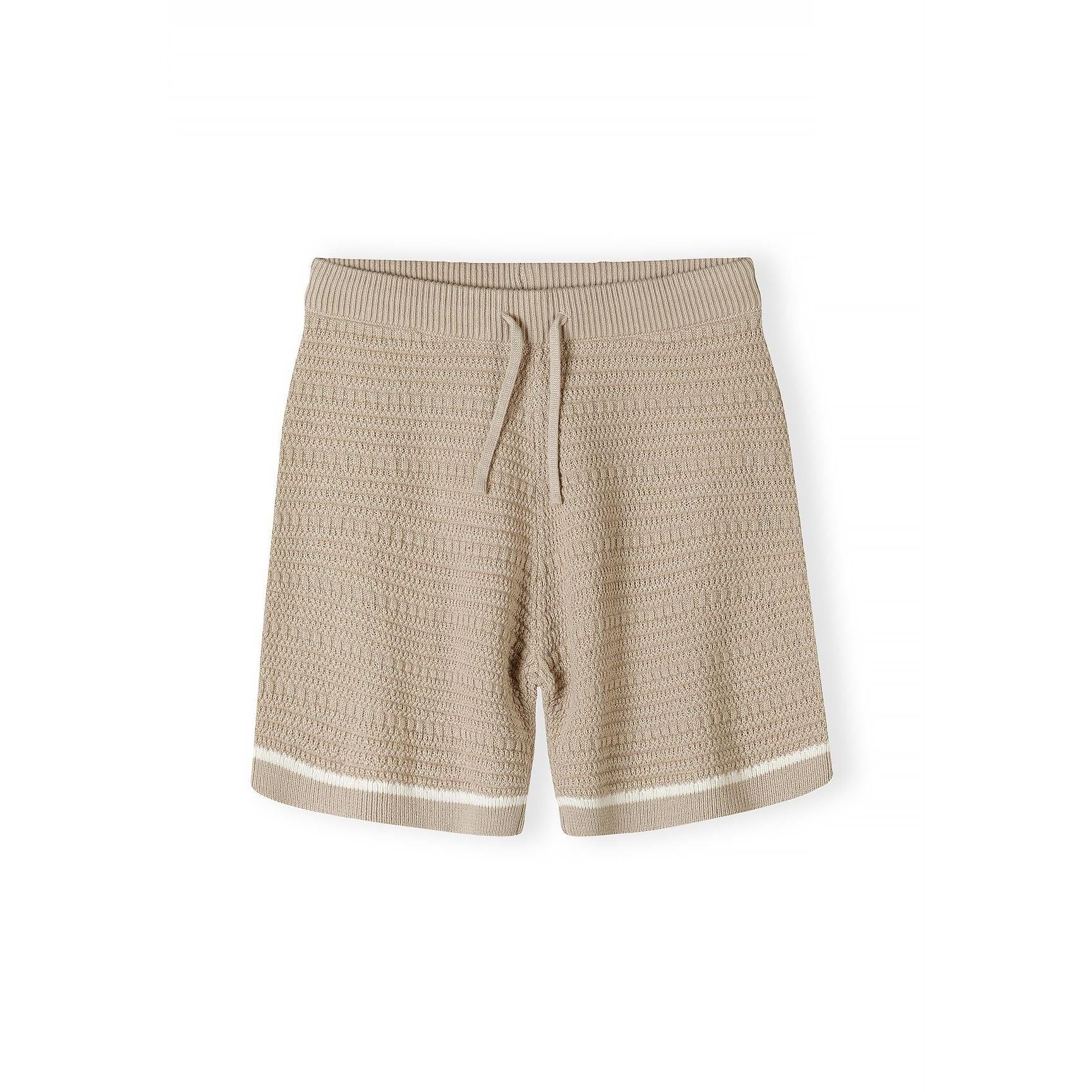 Close-up detail of beige polo shirt showing Minoti label, button placket, chest pocket and herringbone knit texture