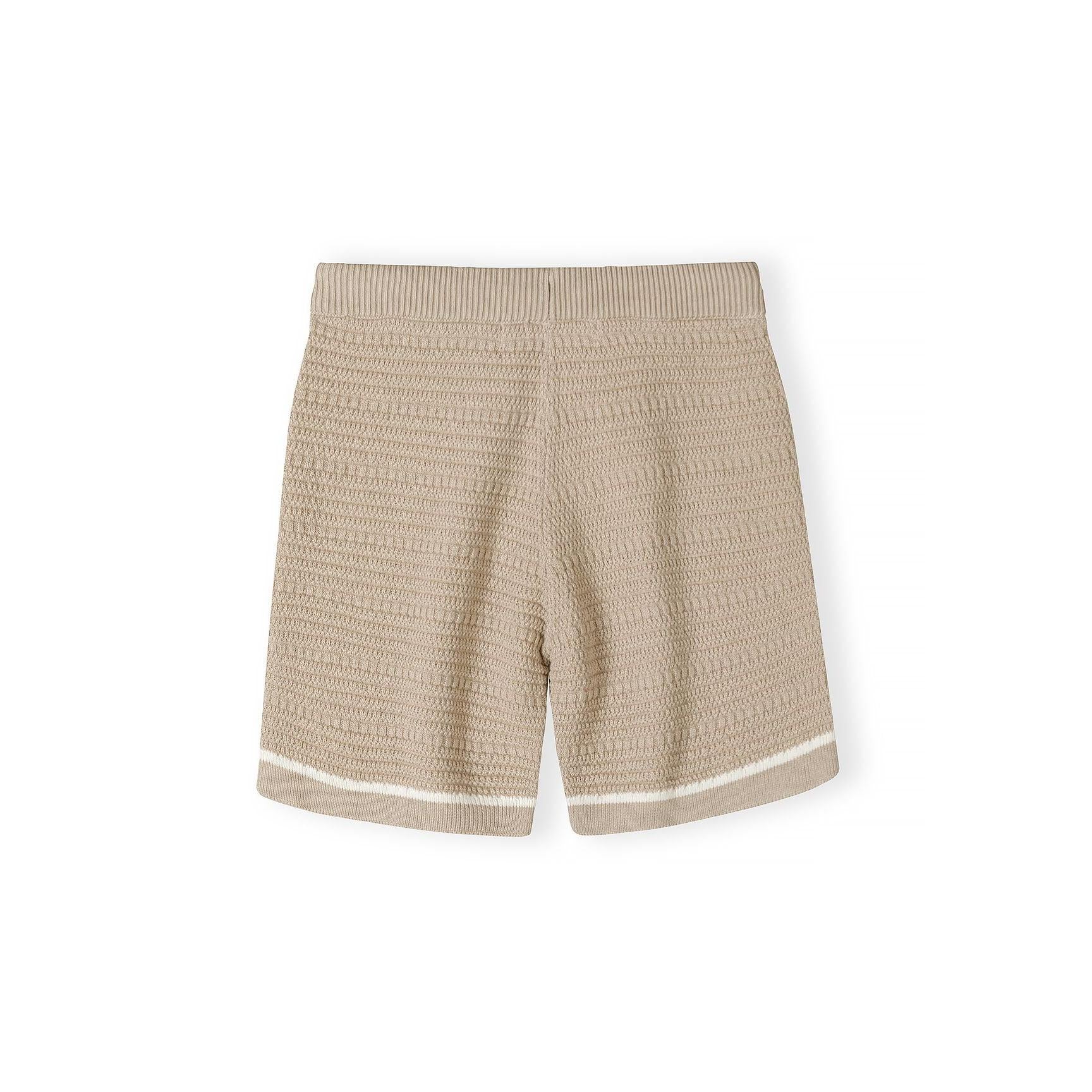 Close-up detail of beige polo shirt showing Minoti label, button placket, chest pocket and herringbone knit texture