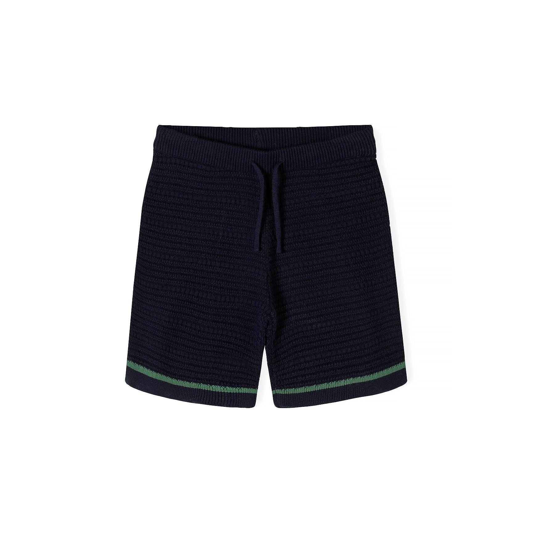 Close-up detail of navy blue knitted polo shirt showing Minoti label, button placket, chest pocket with green piping trim