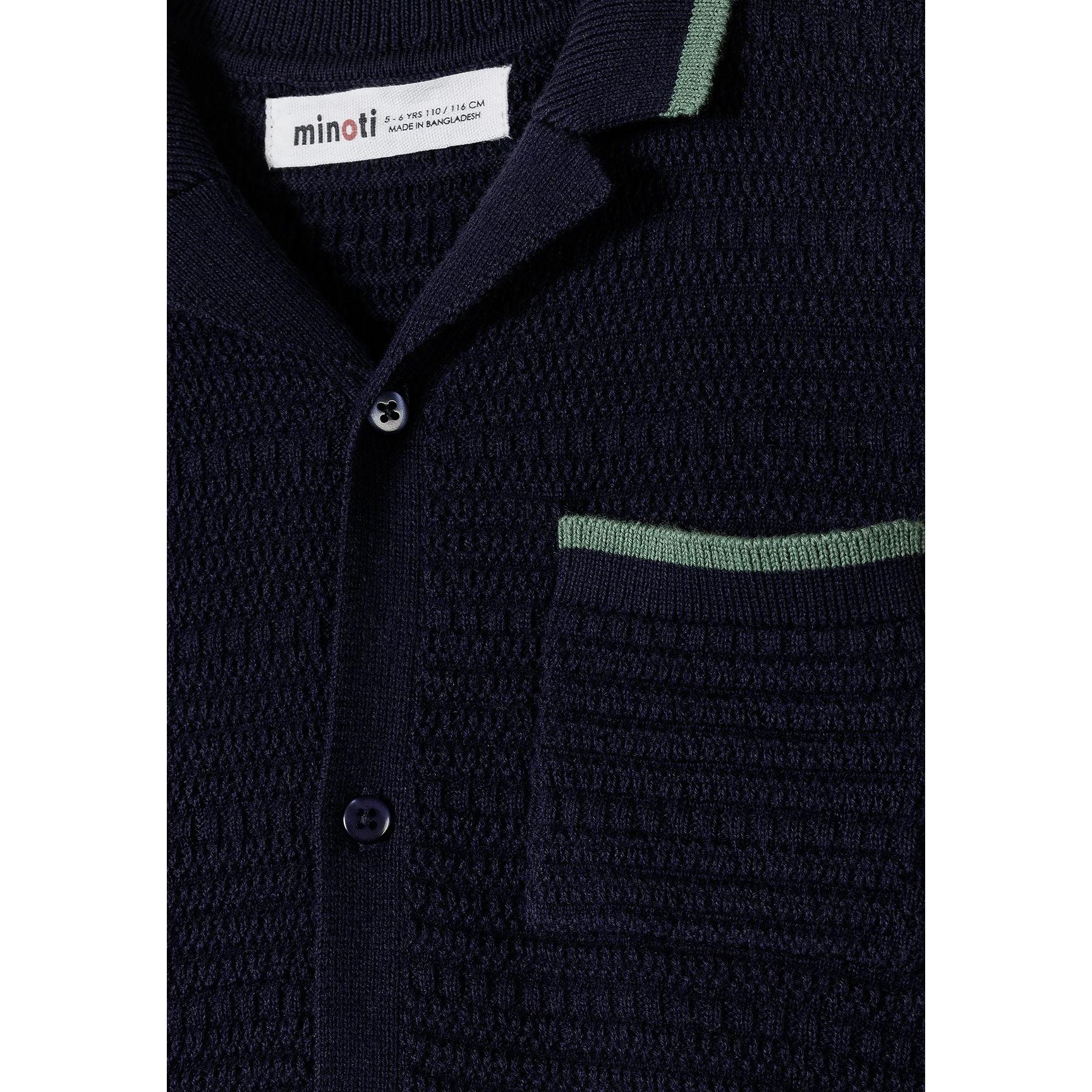 Close-up detail of navy blue knitted polo shirt showing Minoti label, button placket, chest pocket with green piping trim