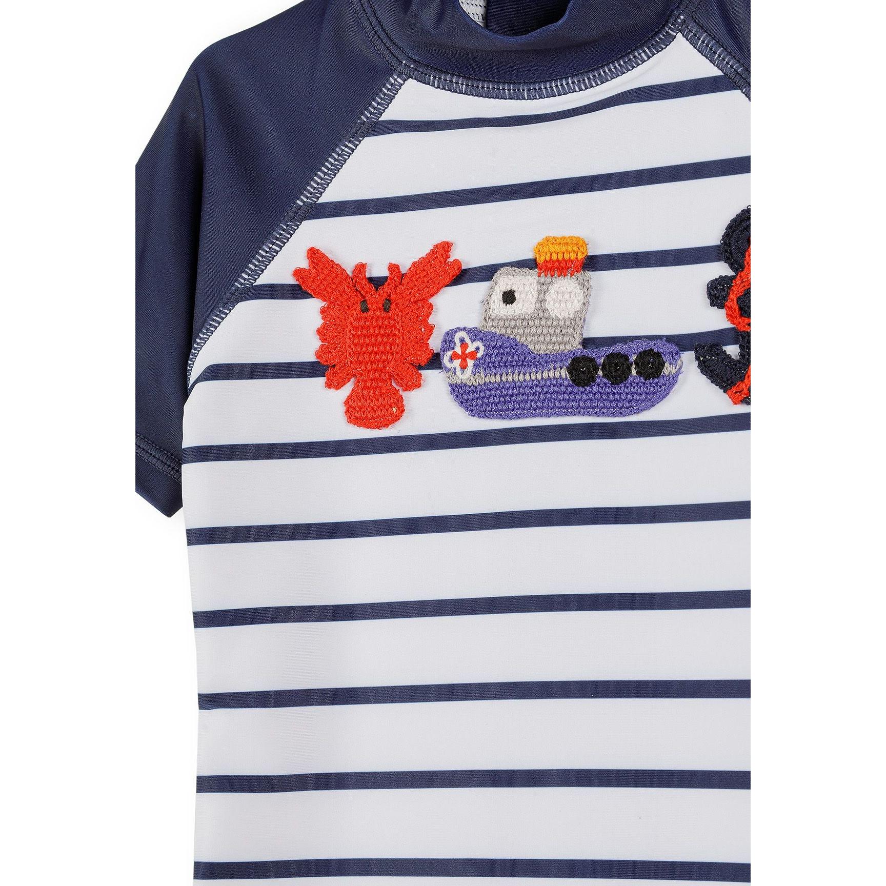 Close-up detail of embroidered appliqués showing red crab and purple boat with anchor on striped fabric background