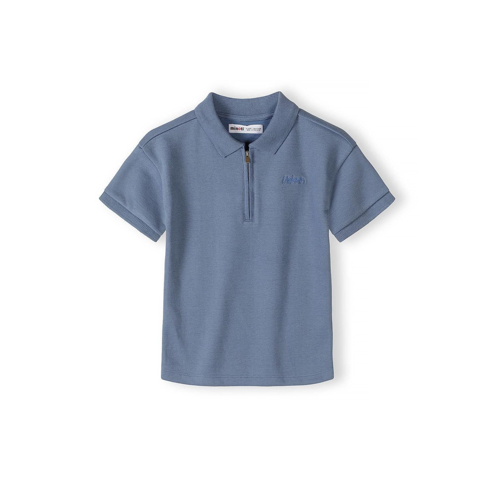 Close-up detail of blue polo shirt showing zip collar, embroidered Minoti logo, and pique texture with brand label visible