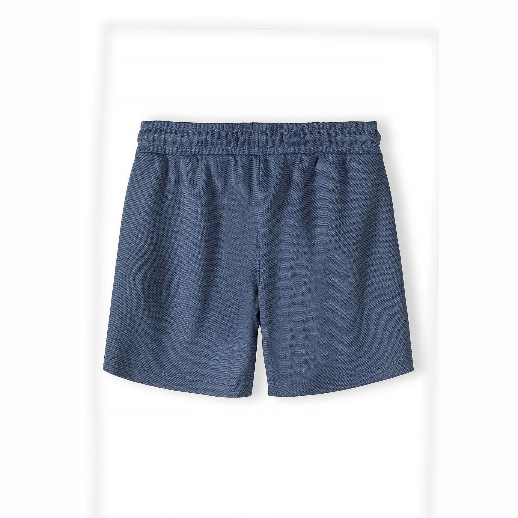 Close-up detail of navy blue pique polo shirt showing Minoti label, zip fastening and colour-block design with textured fabric