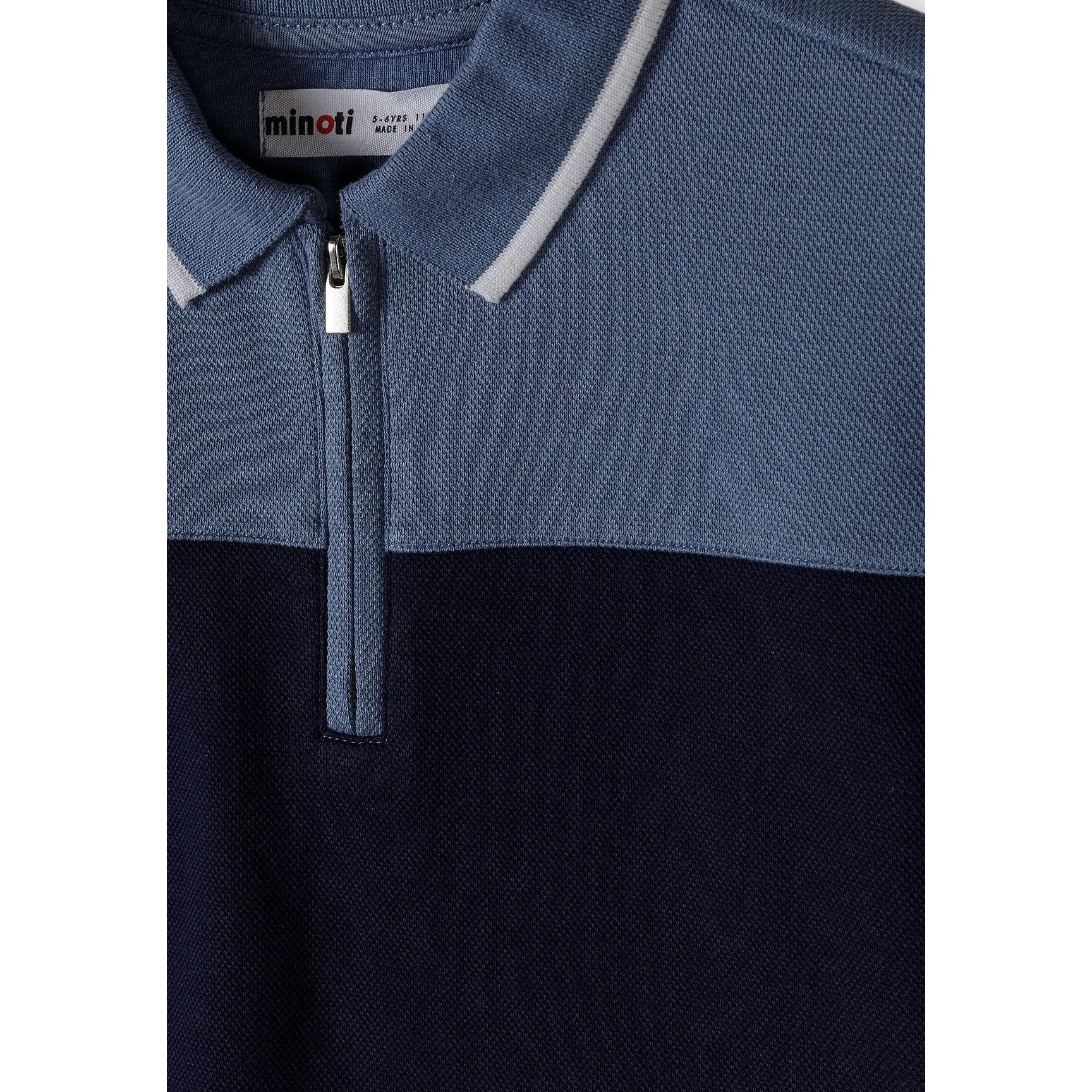 Close-up detail of navy blue pique polo shirt showing Minoti label, zip fastening and colour-block design with textured fabric