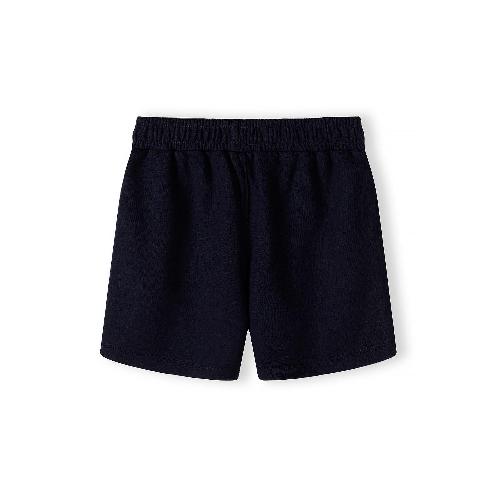 Close-up detail of cream pique polo shirt showing Minoti label, zip neck opening, navy collar and subtle embroidered logo on chest