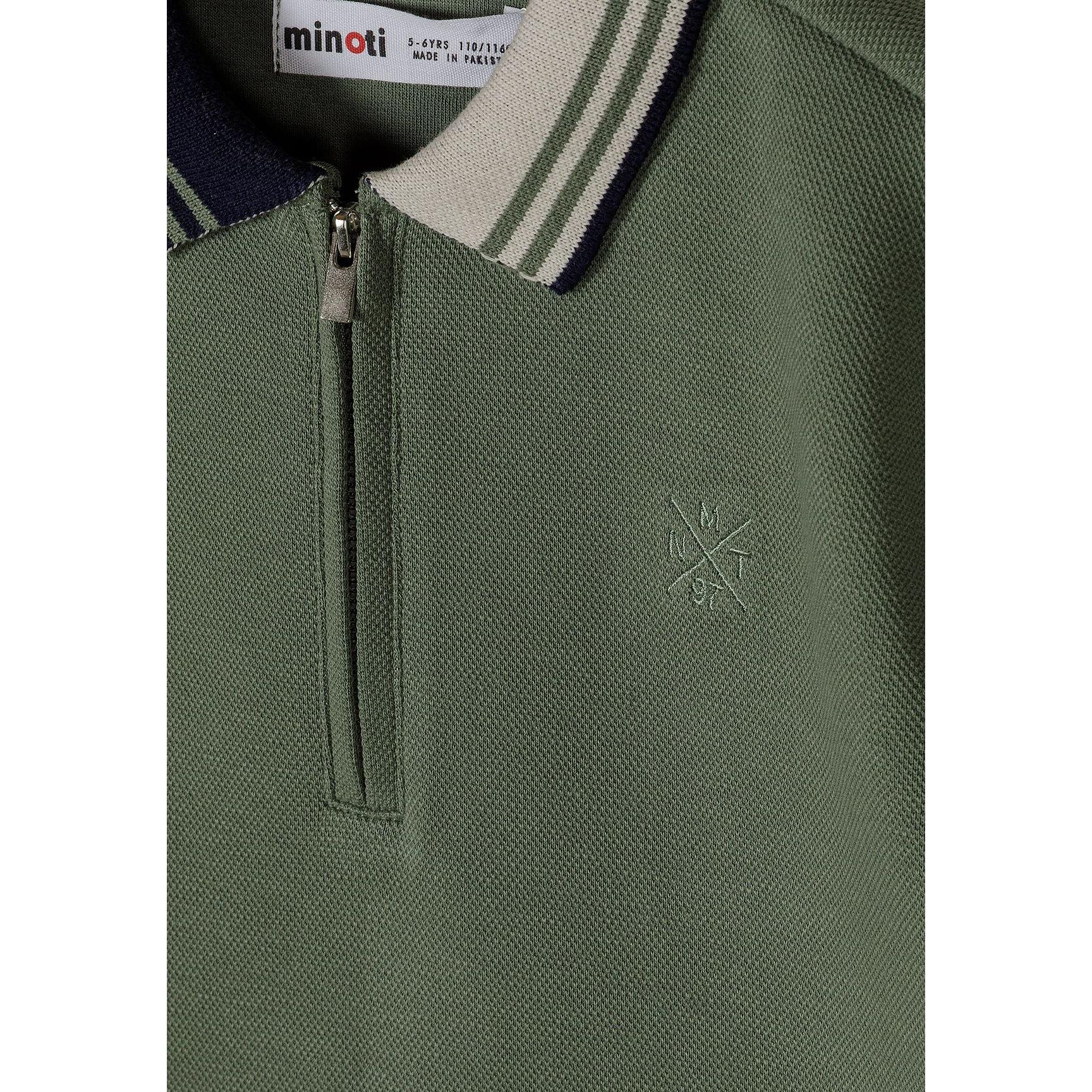 Close-up detail of teal polo shirt showing Minoti label, half-zip closure, contrast collar trim and embroidered star logo