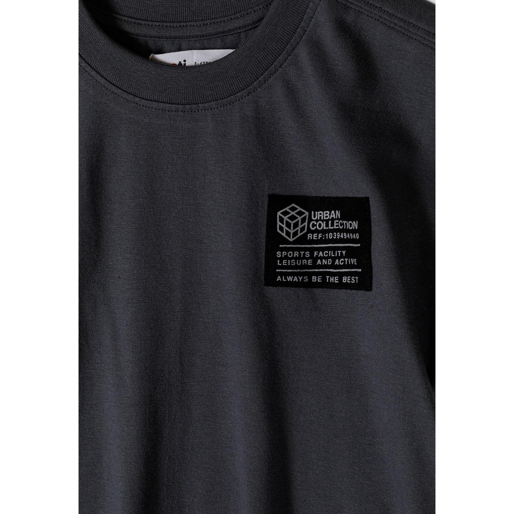 Close-up detail of urban collection patch on grey t-shirt featuring geometric cube logo and text